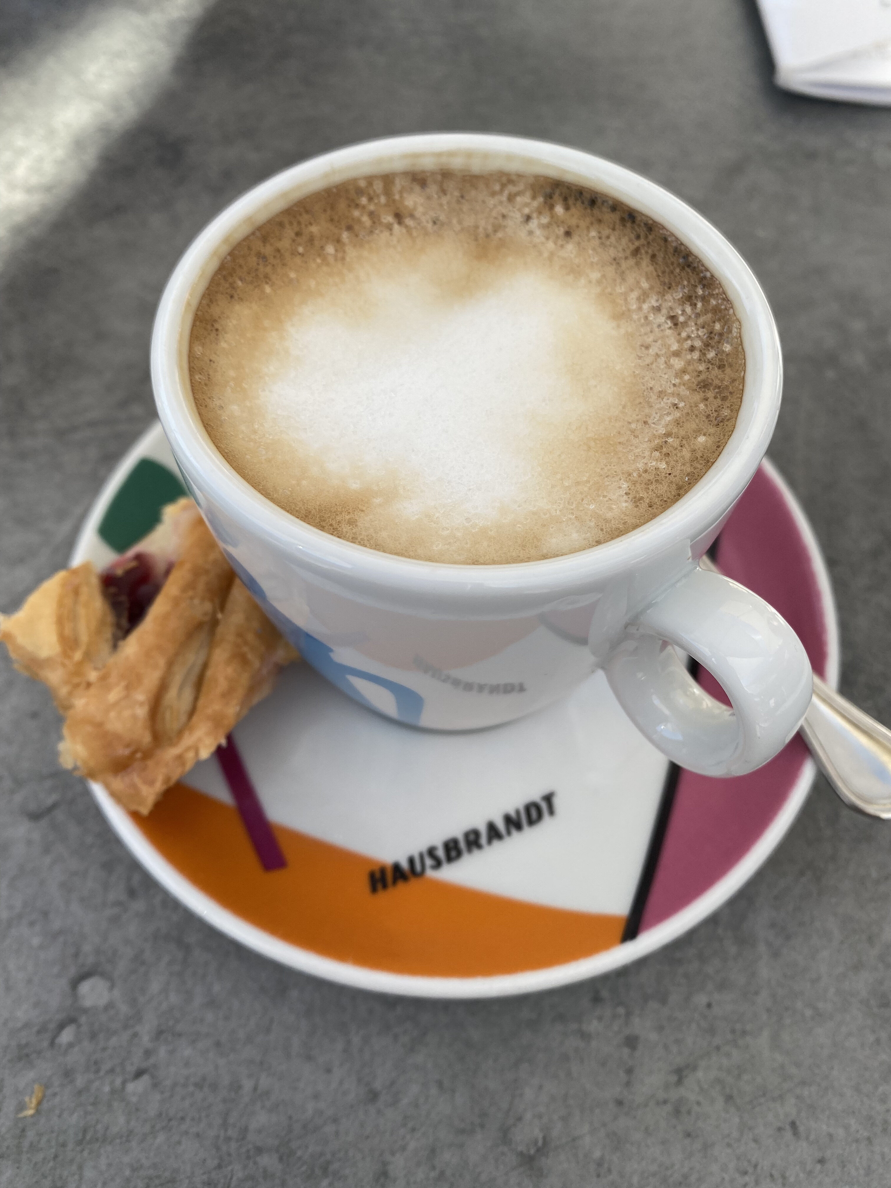 A perfectly-made Italian cappuccino on a small plate with a biscuit.