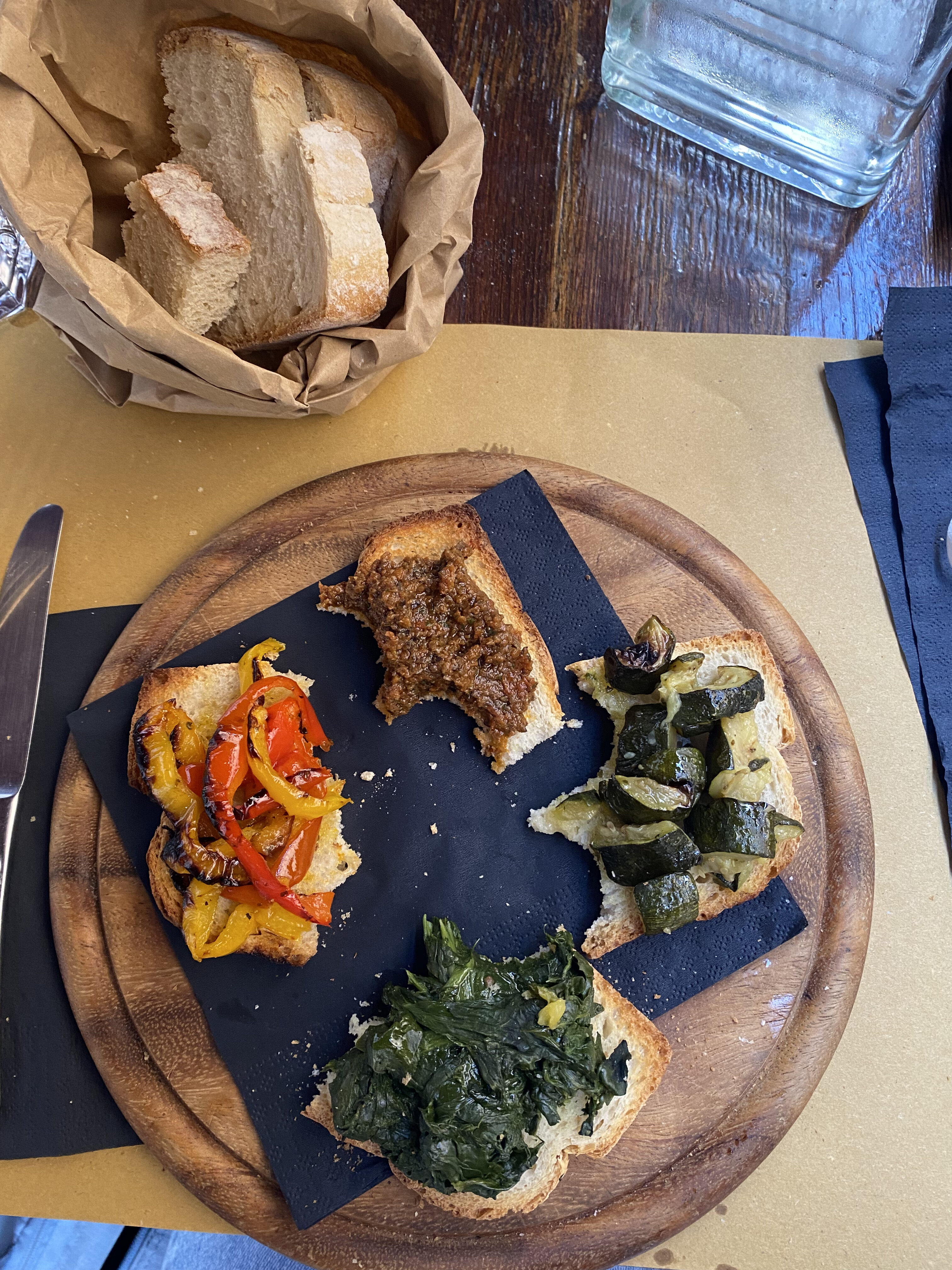 A group of half eaten bruschetta on a wooden plate with a bag of bread near the plate.