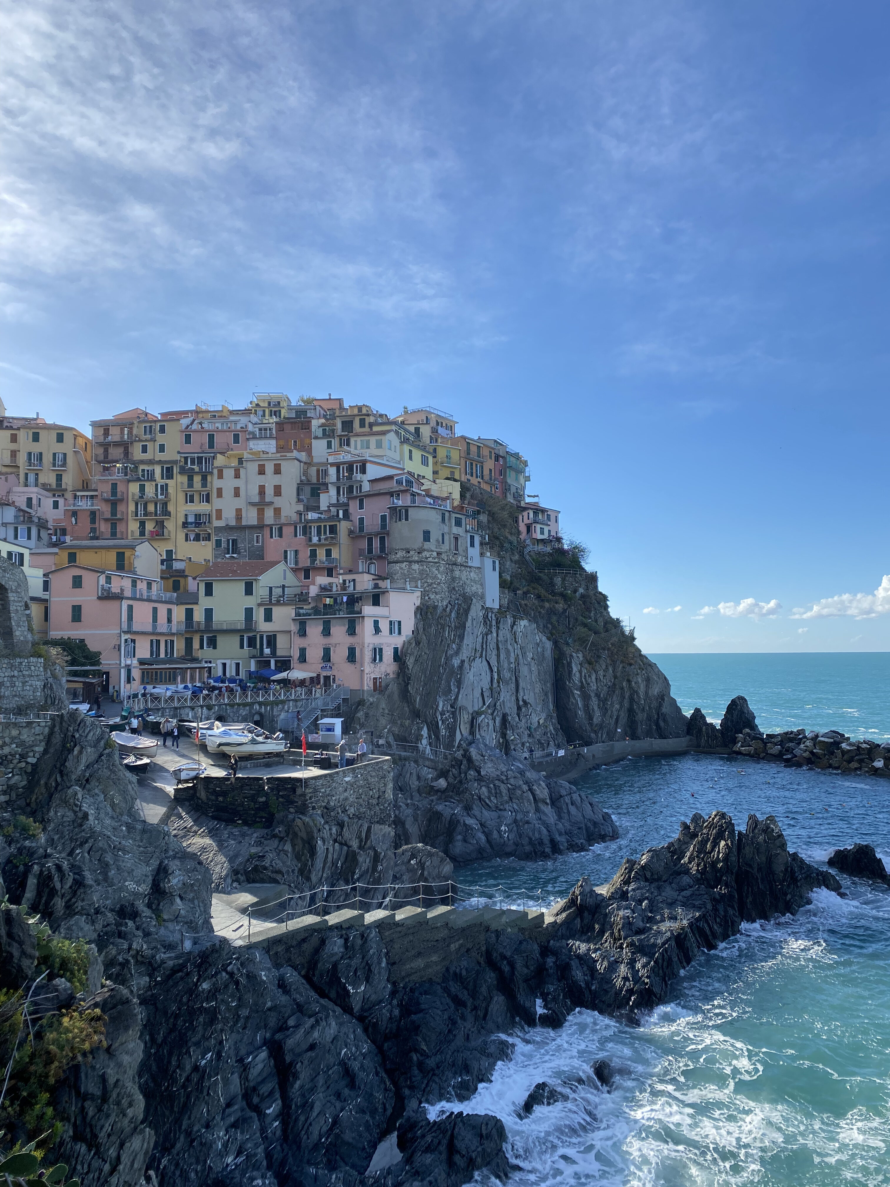 One of Cinque Terre's most picturesque cliffside towns, featuring colorful architecture, a rocky sea below, and a bright blue sky that blends into the deep blue of the ocean surrounding it. 
