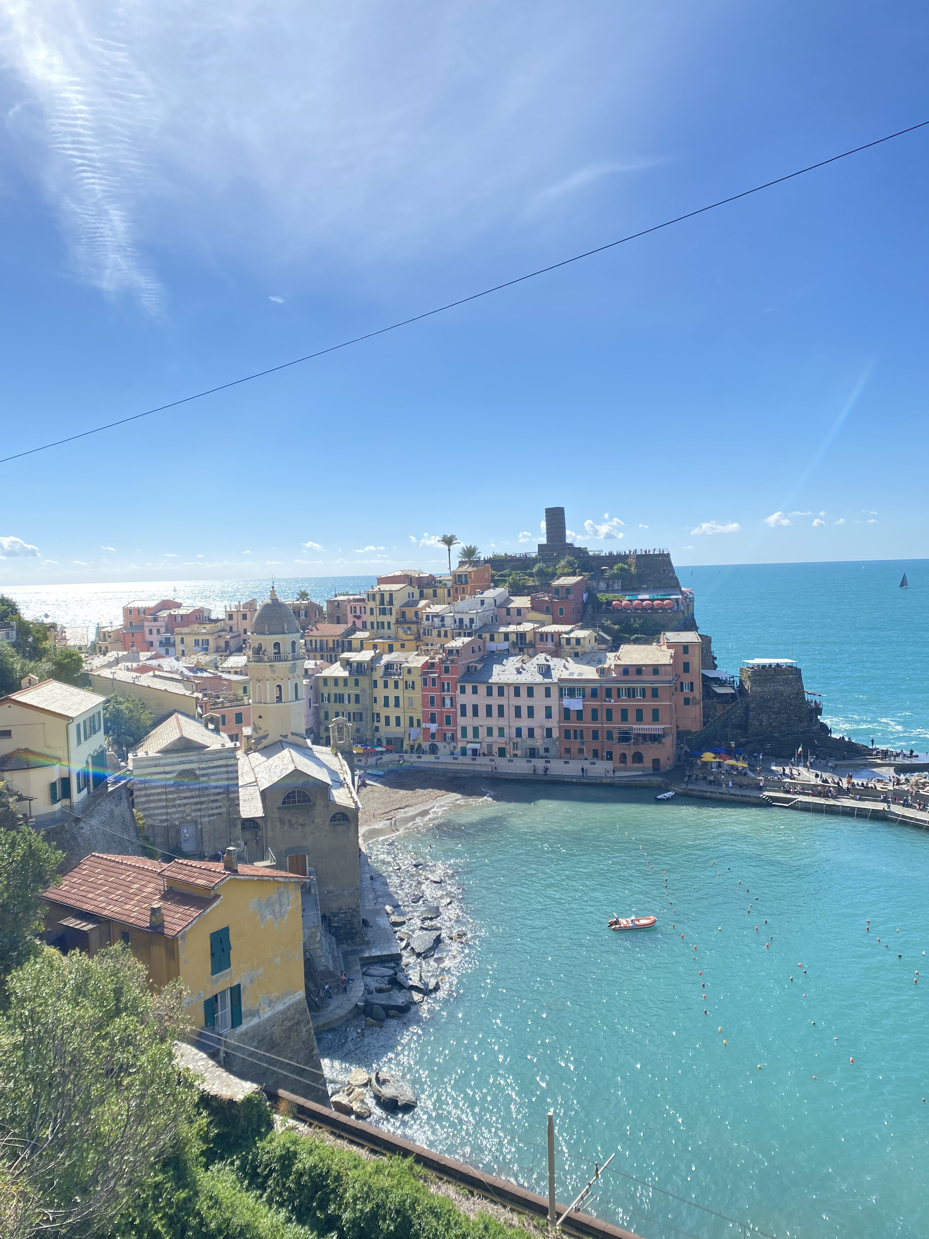 The amphitheater-shaped town of Vernazza, one of Cinque Terre's picturesque cliffside towns which features colorful Italian architecture and a cerulean harbor, surrounded by the deep blue sea and the bright blue sky. 