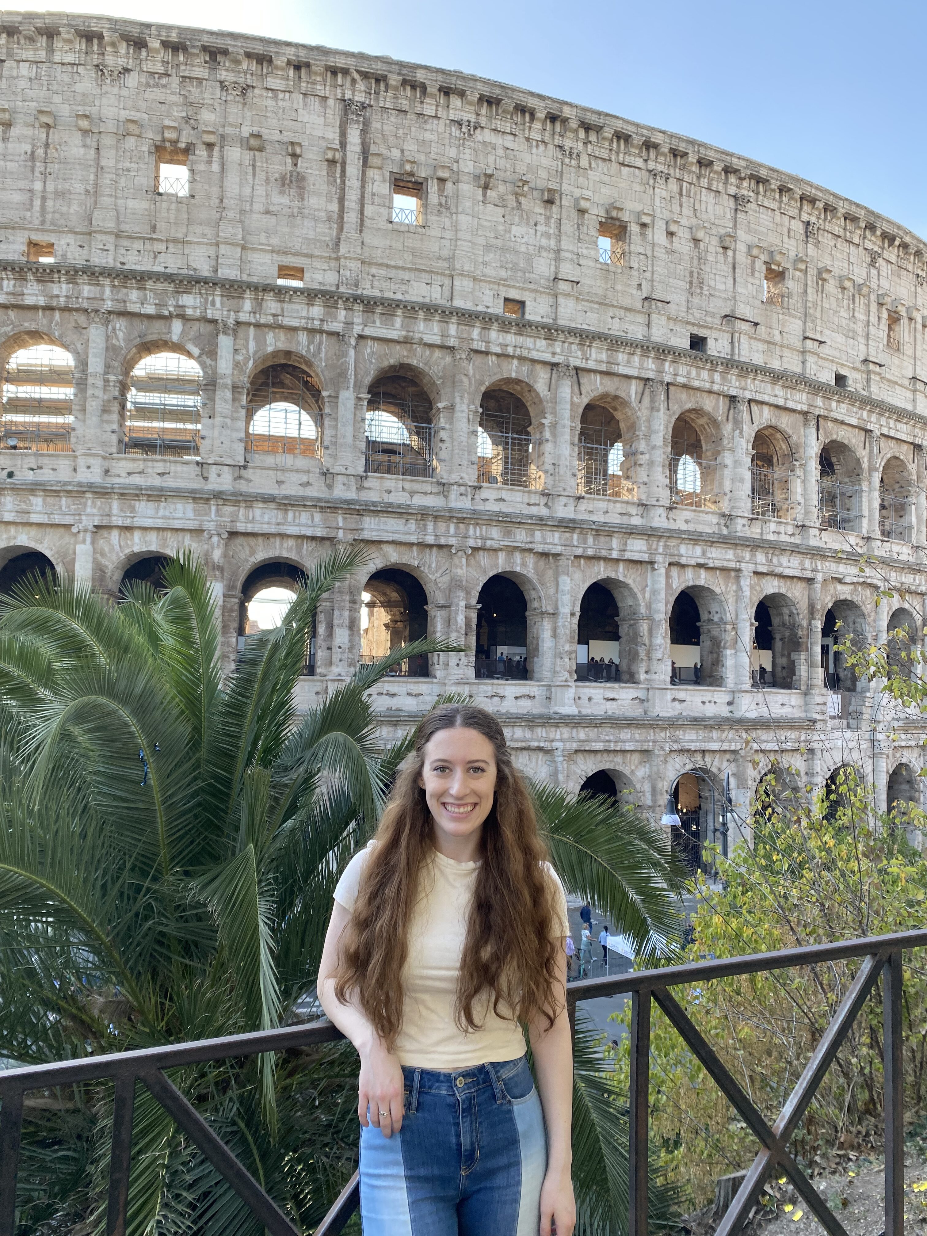 Bella, wearing an off-white crop top and two-toned jeans, stands in front of the Colosseum