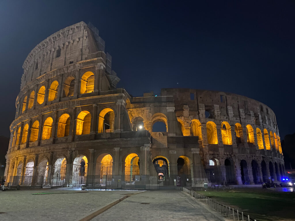 I loved sitting outside the Colosseum as the sun set! Golden lights glow through the arcades of the Colosseum at night, with a dark sky creating an incredible night scene of the Colosseum in Rome.