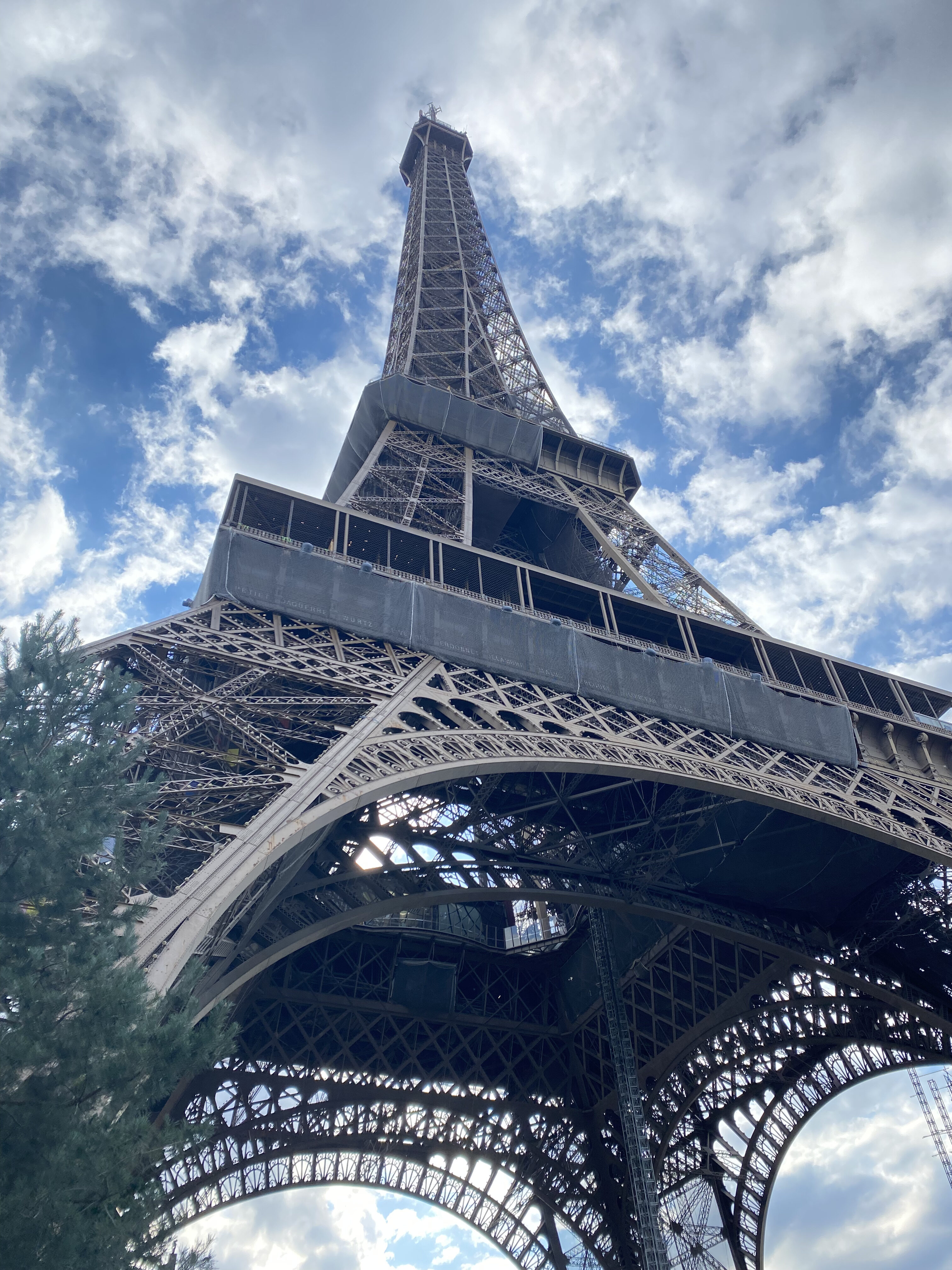The Eiffel Tower, seen from beneath the monumental structure, with a cloudy blue sky decorating the background.
