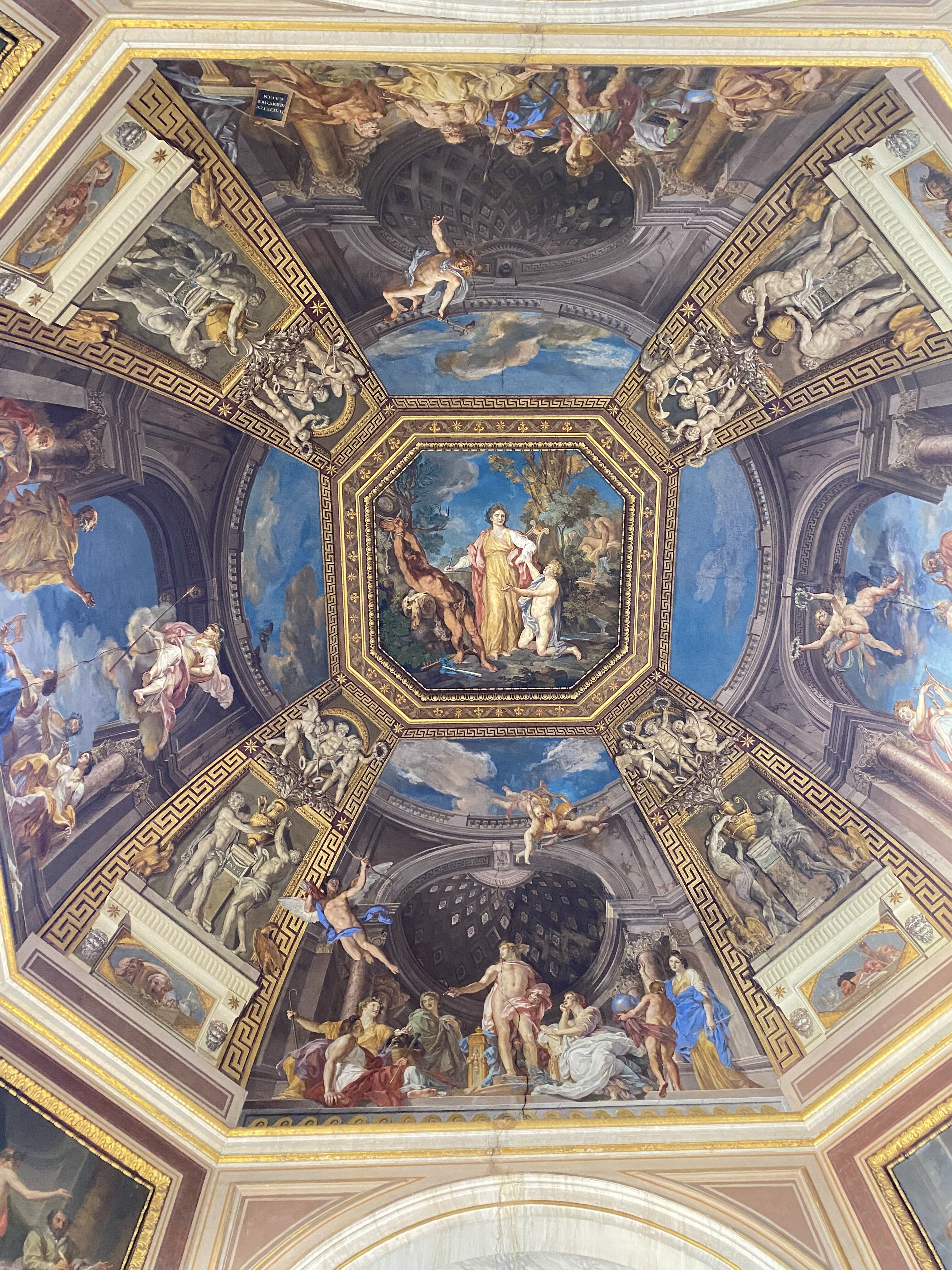 An ornately decorated ceiling with a biblical scene the center, extending outward via golden geometric patterns which feature angels all around the domed ceiling.