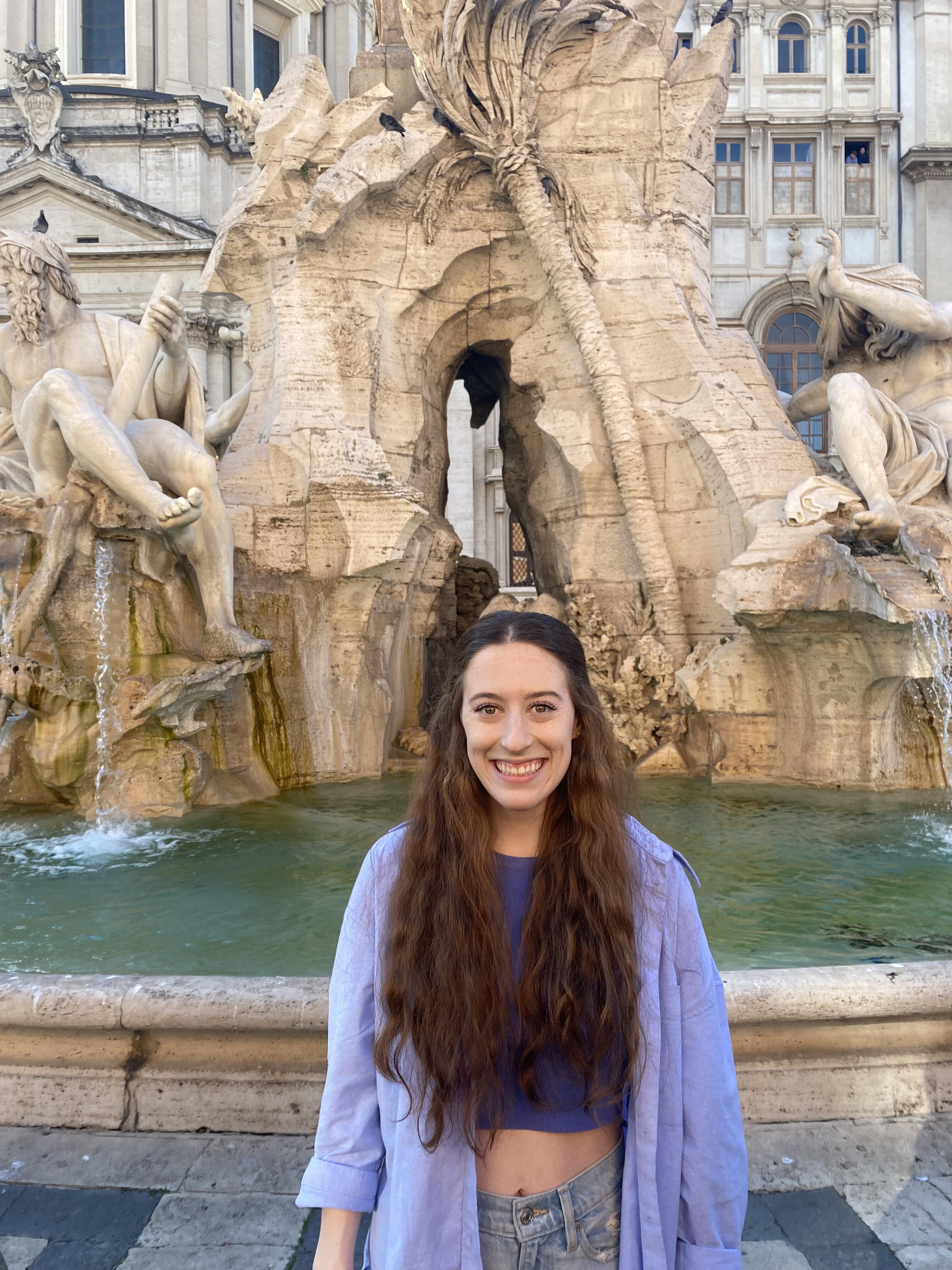 I highly recommend staying near Piazza Navona when you visit Rome! A young women in blue (Bella) standing in front of a sculptural fountain featuring two carved males.