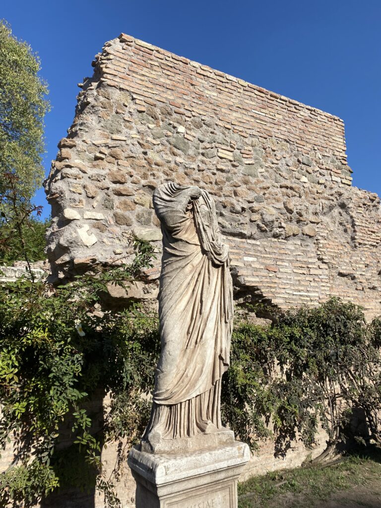 The ancient ruins of a headless statue in front of a weathered brick wall in Rome.