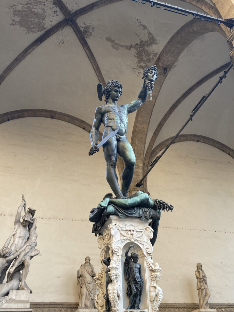 A bronze sculpture, turned green by weather, of Perseus slaying Medusa. This sculpture is outside Palazzo Vecchio within a loggia.