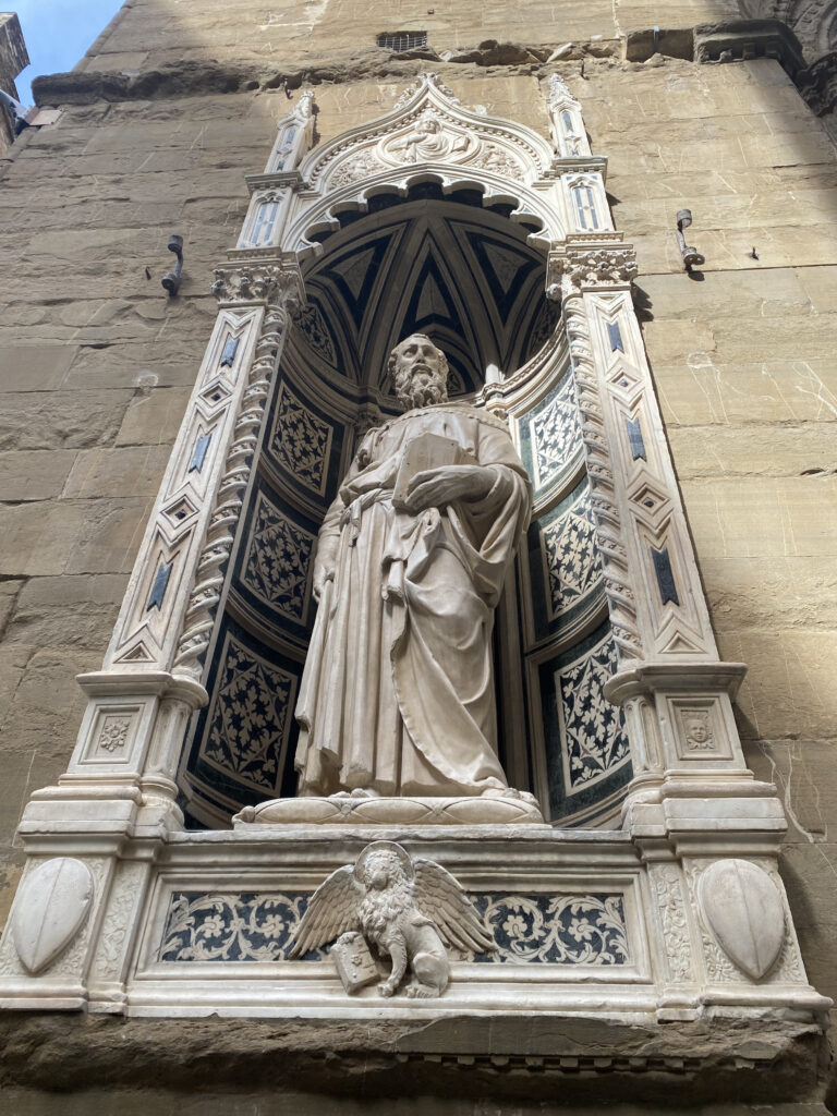 A white stone sculpture set in a niche on the weathered stone building of Orsanmichele.