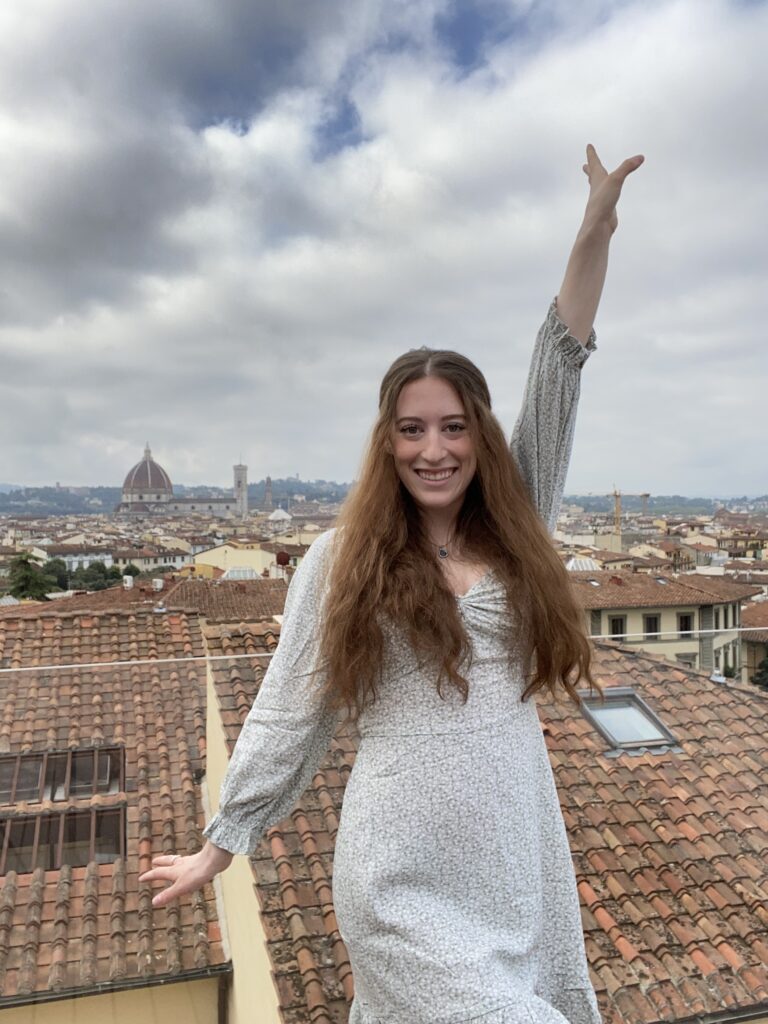 Bella posing with one arm up and the other down in front of the burnt orange Florentine skyline.
