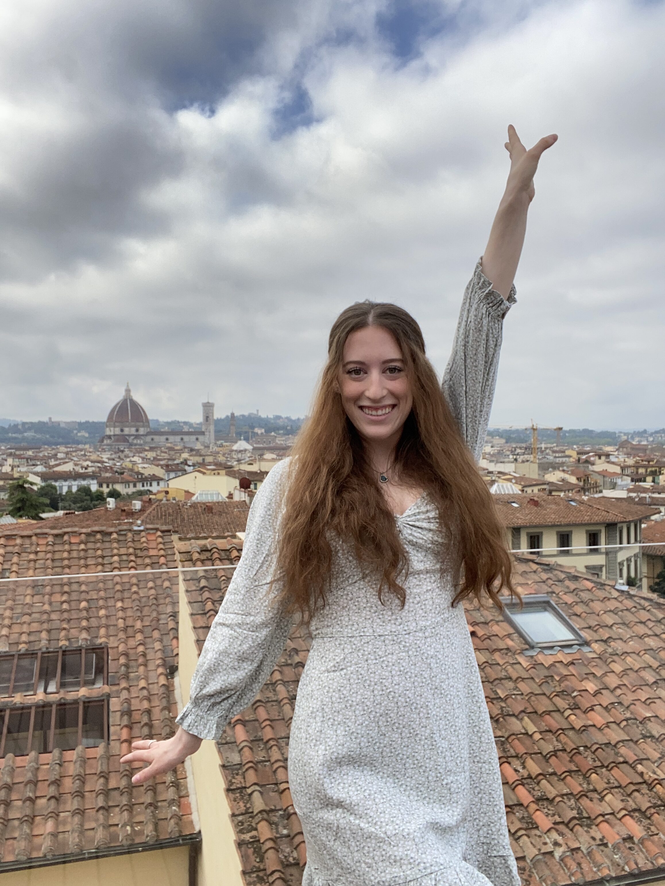 Bella posing with one arm up and the other down in front of the burnt orange Florentine skyline.