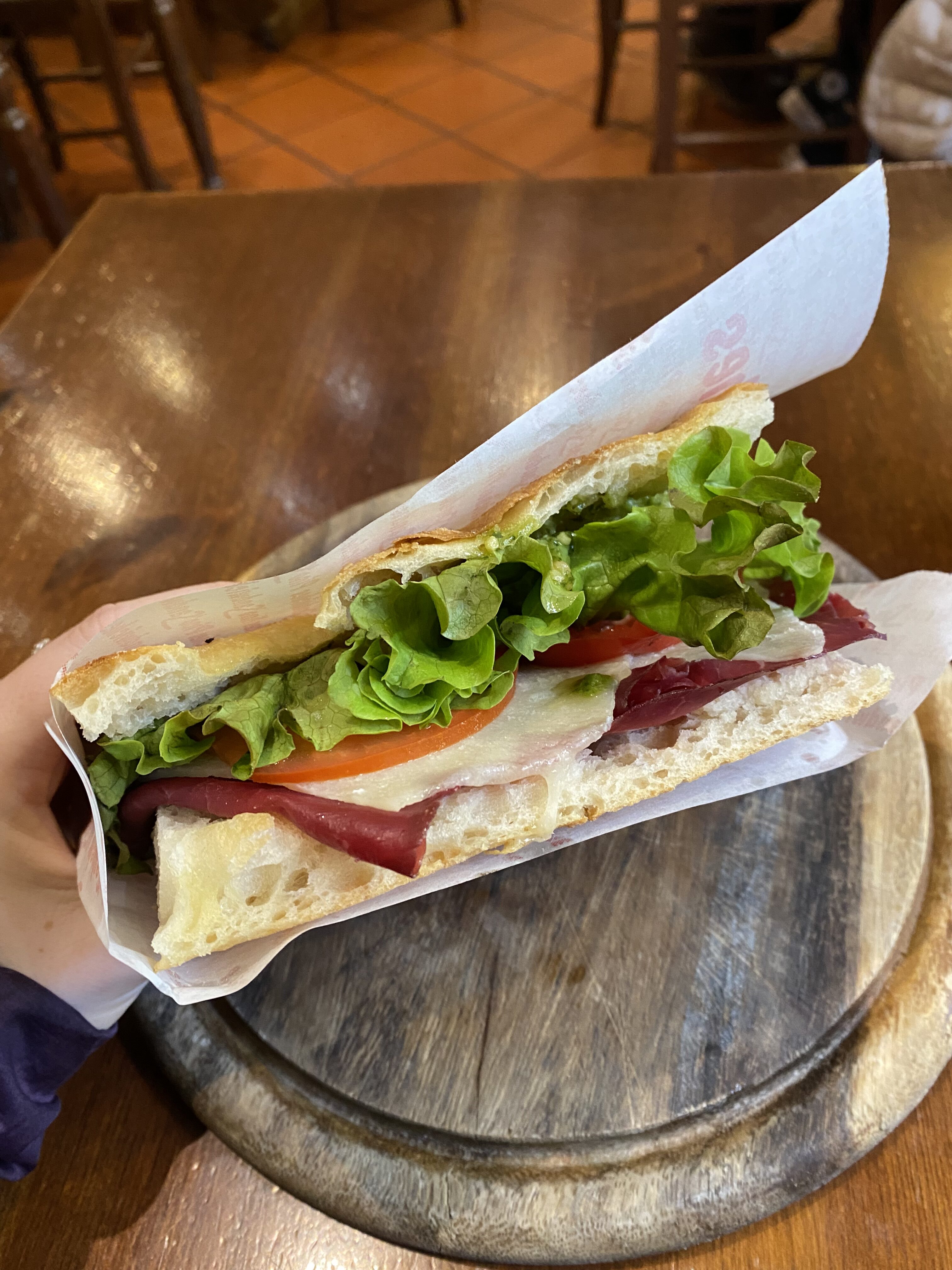 A Florentine sandwich with arugula, bresaola and other sandwich fixings. A wooden table is shown in the background.