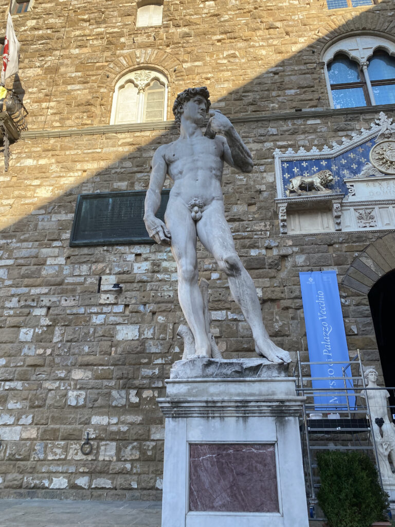 The David replica erected in front of the weather brown stone of the Palazzo Vecchio.
