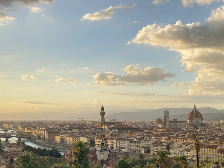 A beautiful Florentine skyline at sunset, seen from the steps of Piazzale Michelangelo. The sky is just starting to see a rainbow of colors for sunset, and clouds fill the scene.
