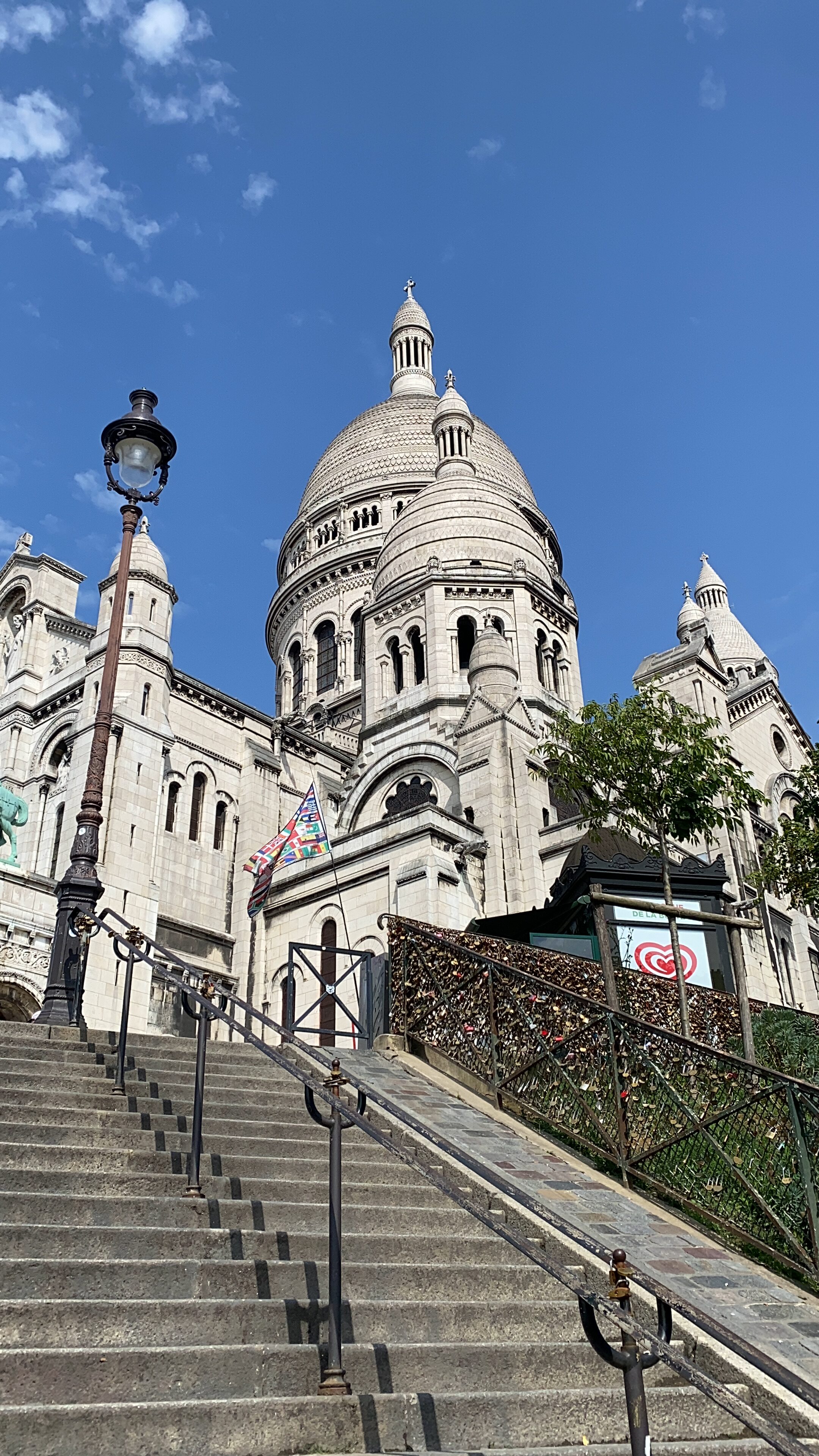 The beautiful Basilique du Sacré-Cœur seen from beneath a staircase in Montmartre. A vibrant blue sky decorates the background.