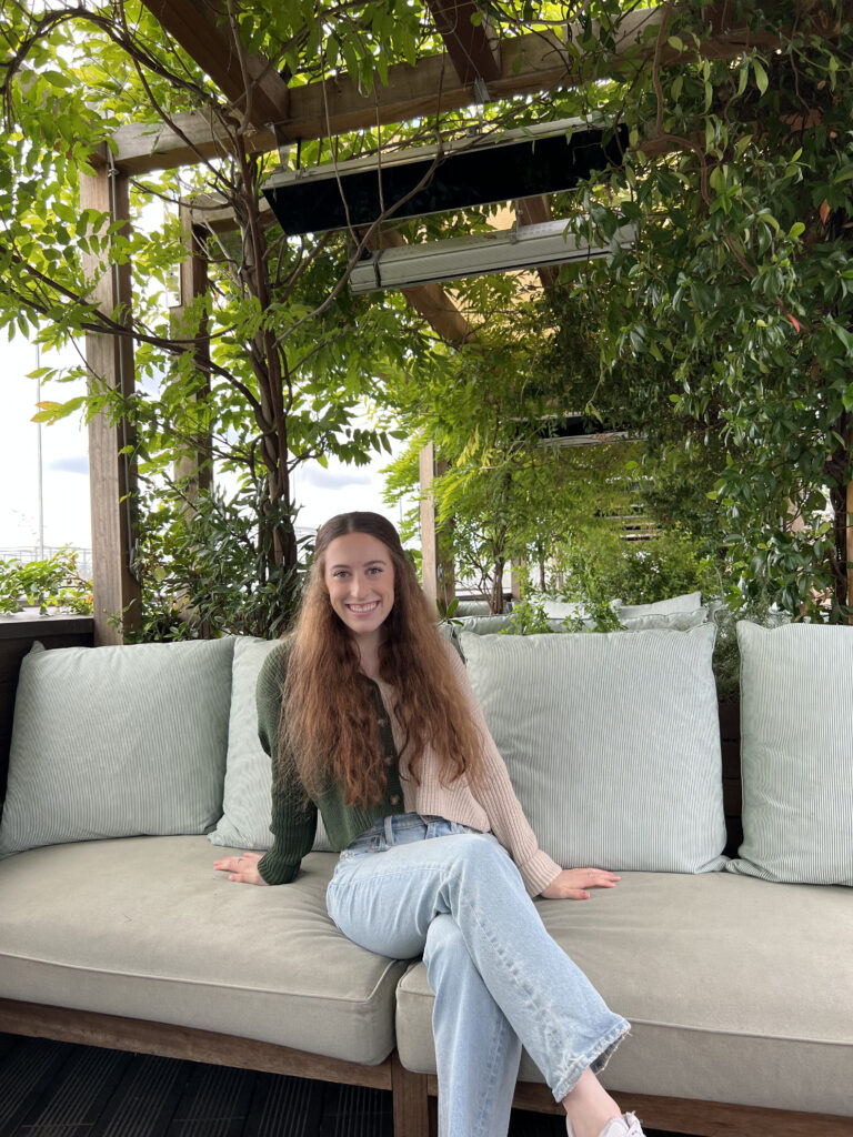 Bella lounging on an outdoor couch in Paris, surrounded by vibrant green plants.