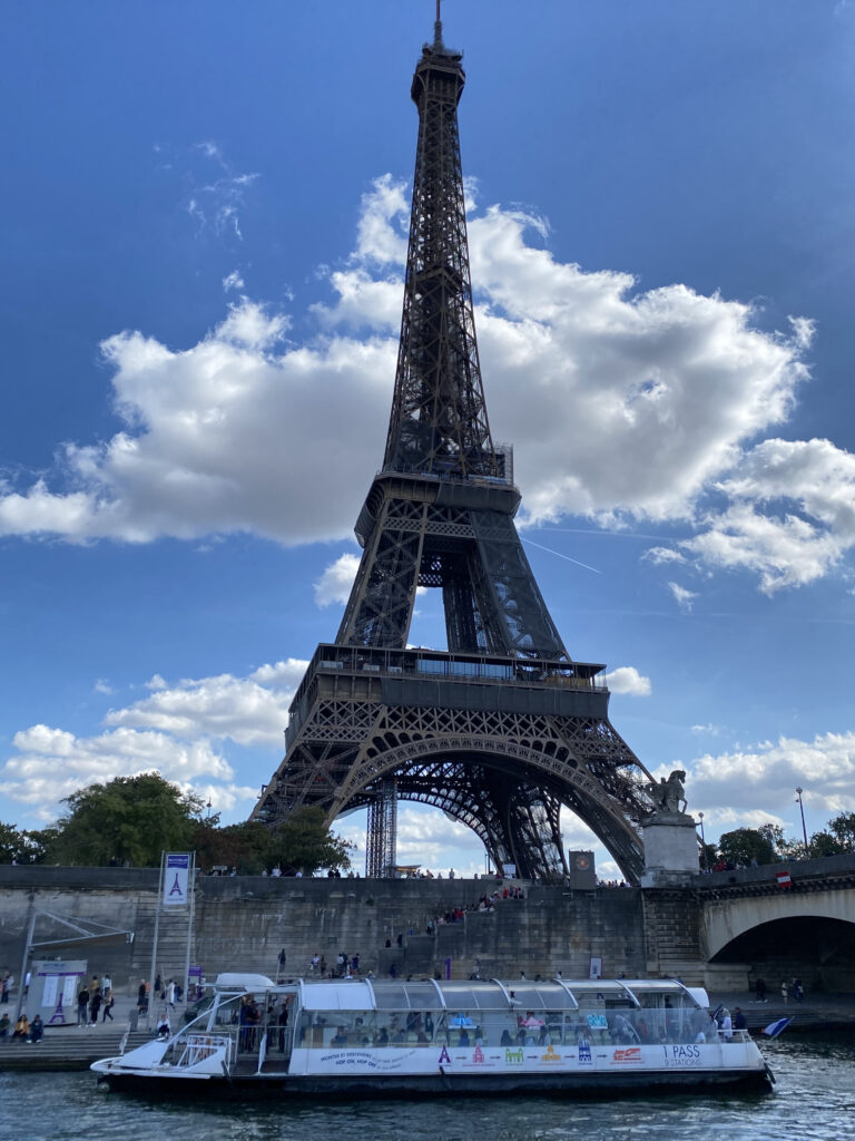 The Eiffel Tower pictured against a partly cloudy sky, with a boat beneath it on the Seine river.