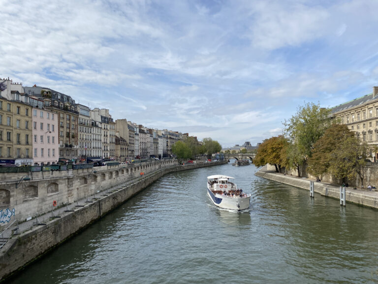The Seine river with beautiful Parisian architecture flanking both sides. A boat glides along the water.