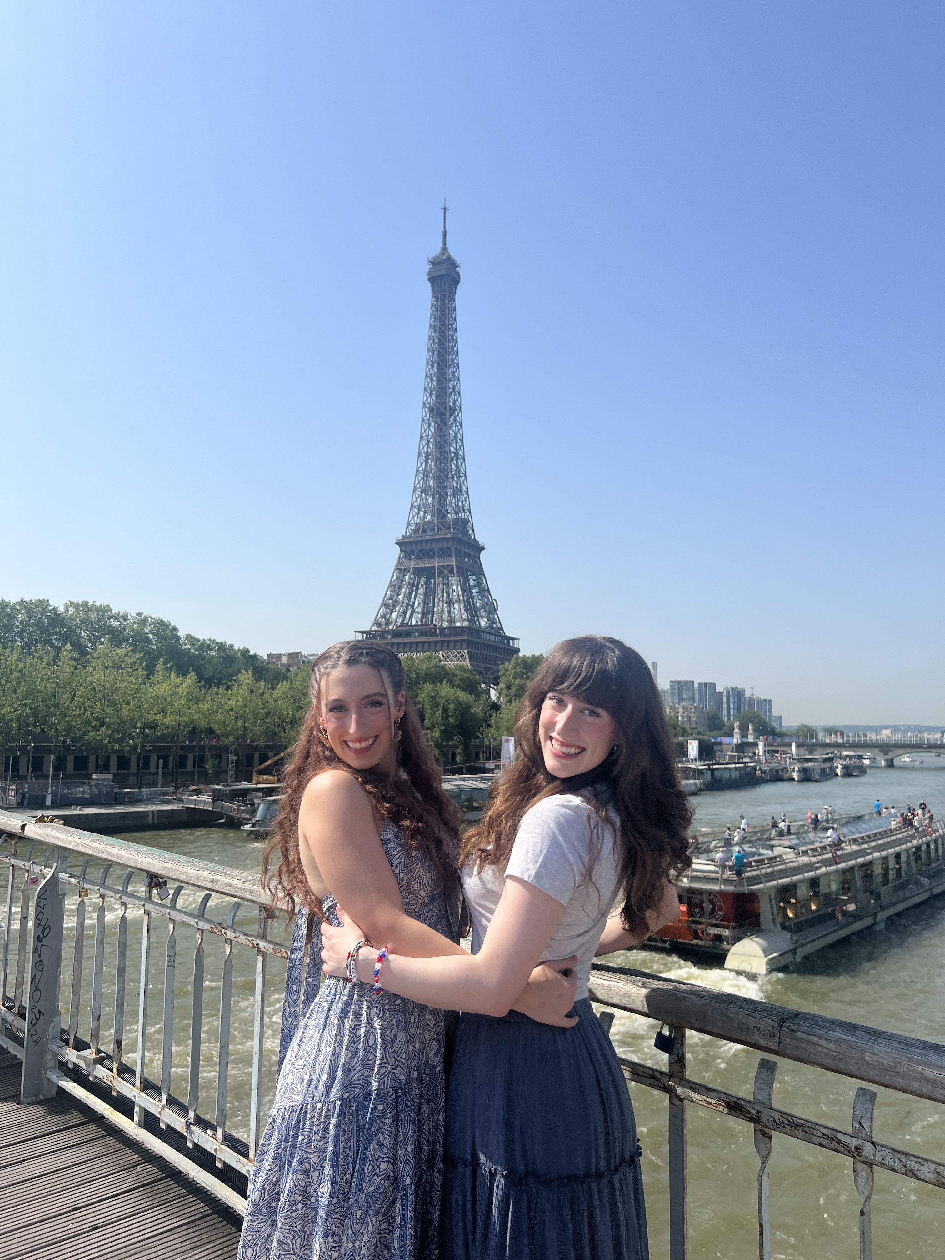 Bella and her twin sister Lily pose on Passerelle Debilly Bridge with the Eiffel Tower and the Seine in the background. Passing along the river is a river cruise tour.