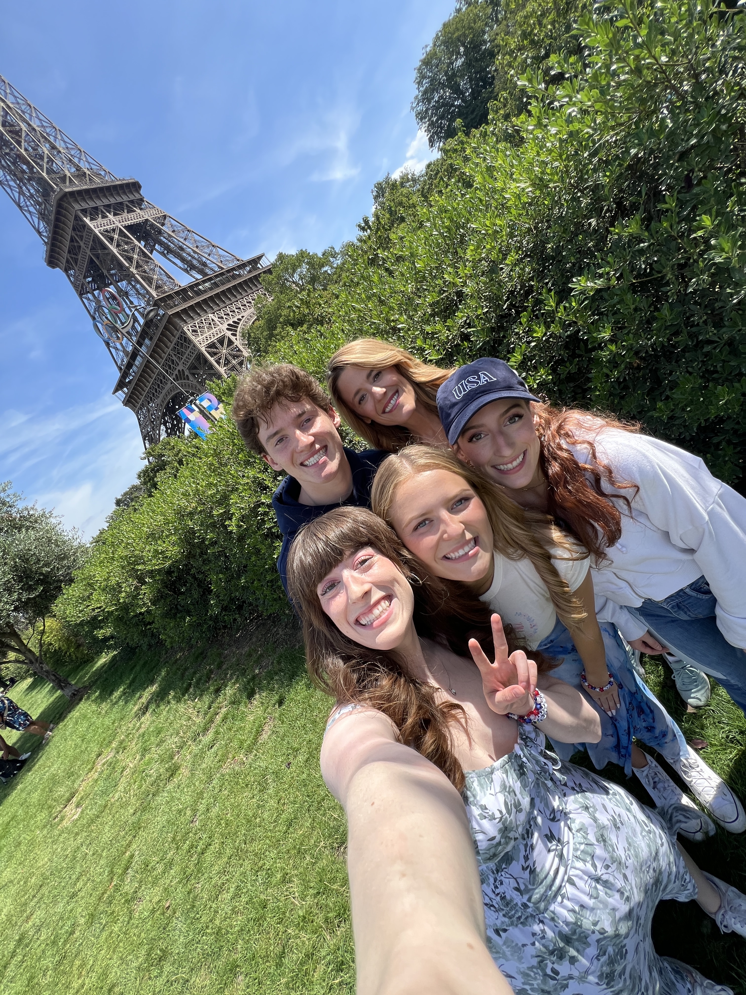 Bella - holding up a peace sign - poses with her family in front of a green park with the Eiffel Tower in the background.