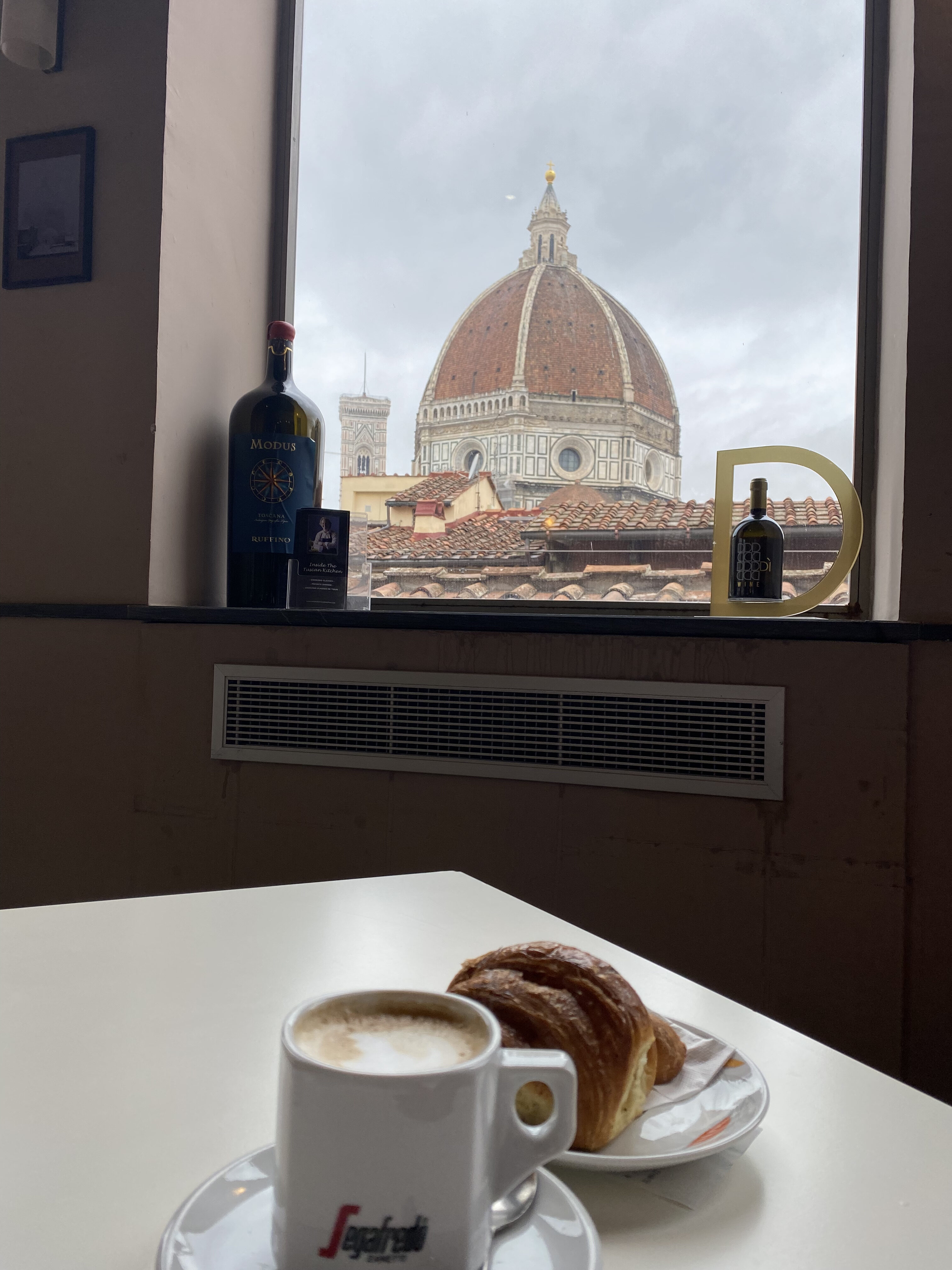 An Italian cappuccino and a fresh pastry on a table in front of a window with a view of the Duomo in Florence.