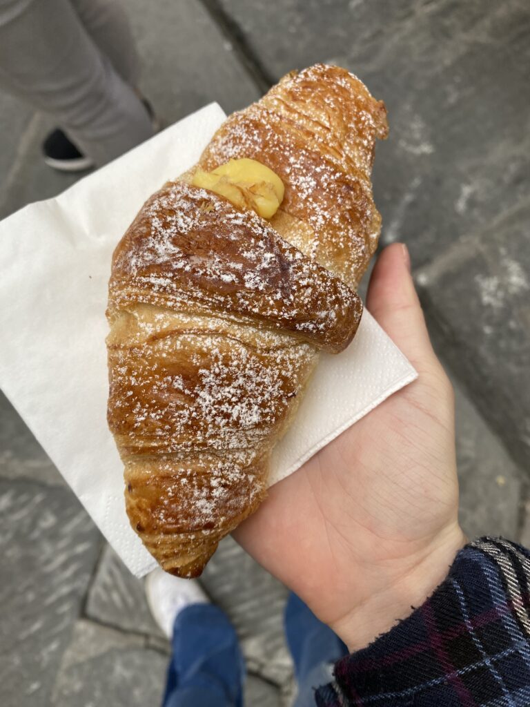 A delectable golden pastry lightly dusted with powdered sugar, with a dollop of yellow custard on top.