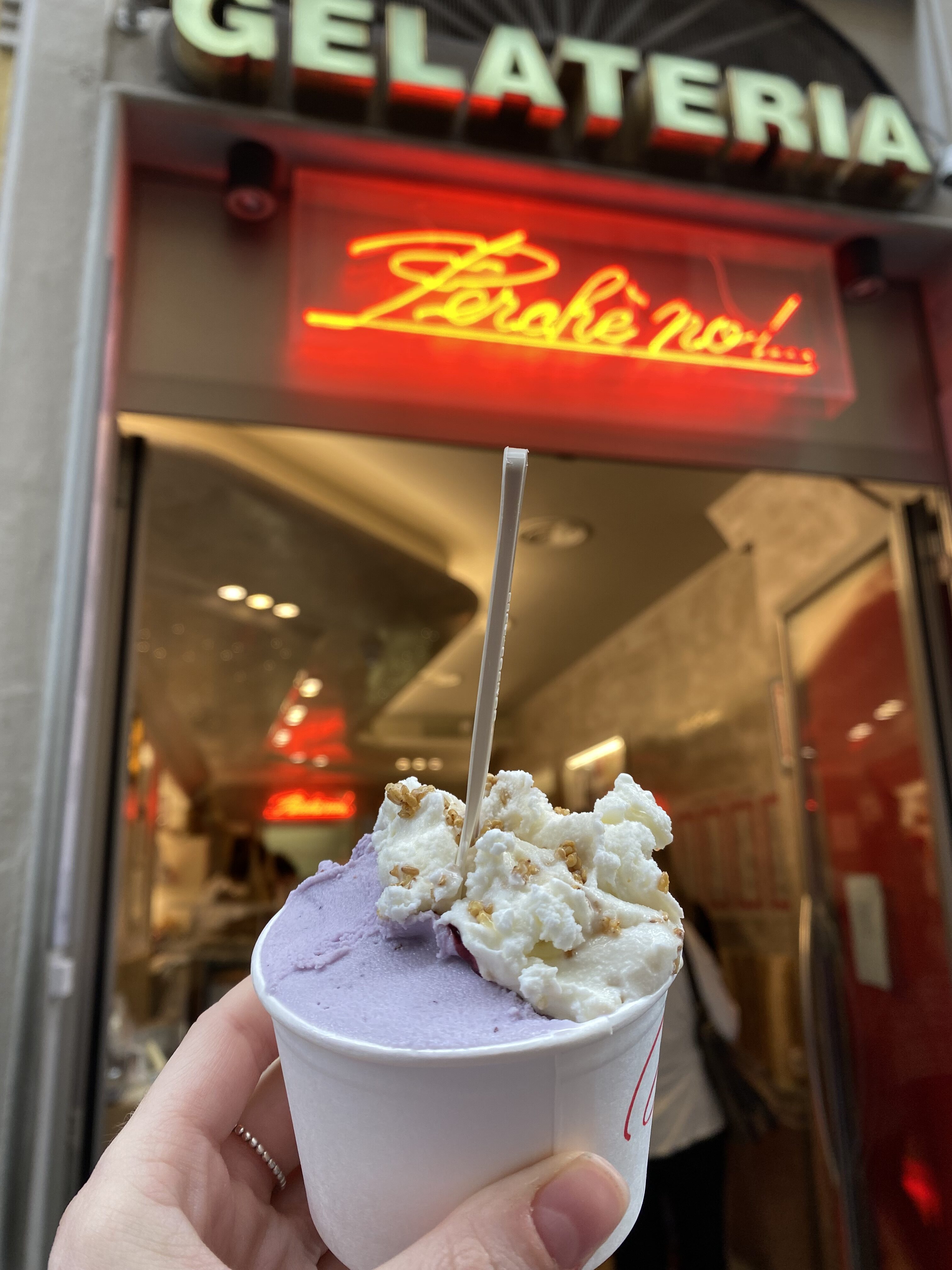 A purple gelato with whipped-cream topping held in from of a sign that says, "Gelateria, Perché No!".