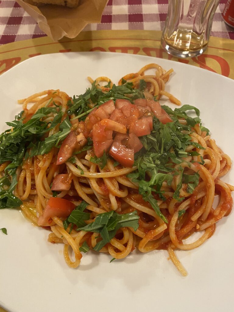 A delicious plate of spaghetti arrabbiata with fresh greens on top. The plate is set upon a red and white gingham tablecloth.