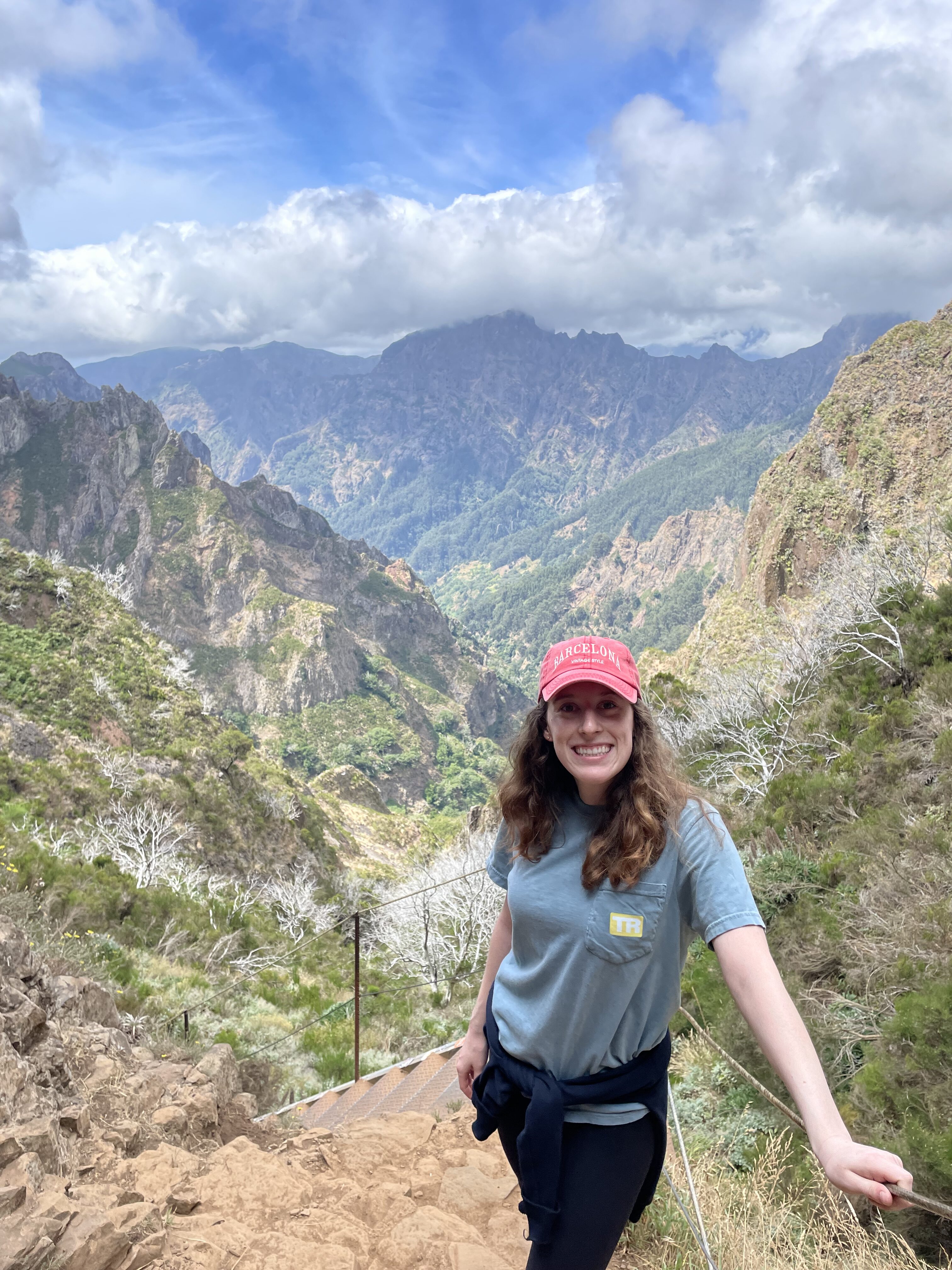 Bella smiling along the Pico Ruivo trail, with jagged green mountains with tan rocky faces in the background.