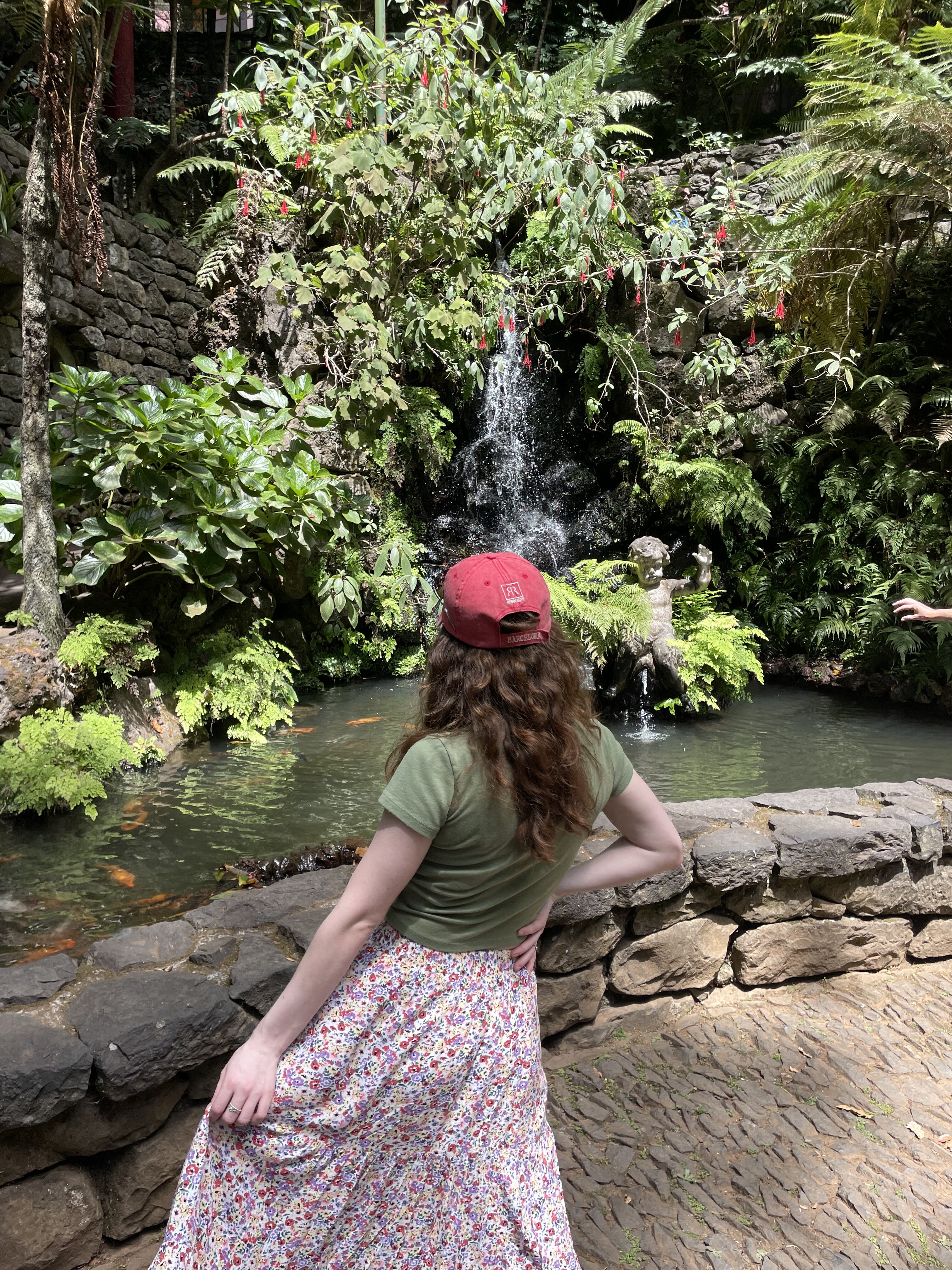Bella grabbing her skirt, facing towards the green scenery posing at Monte Palace Tropical Garden in Monte (Madeira).
