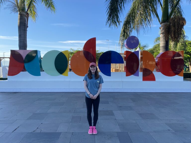 Bella standing in front of a colorful Madeira sign wearing her hiking gear (blue t-shirt, black leggings and pink tennis shoes).