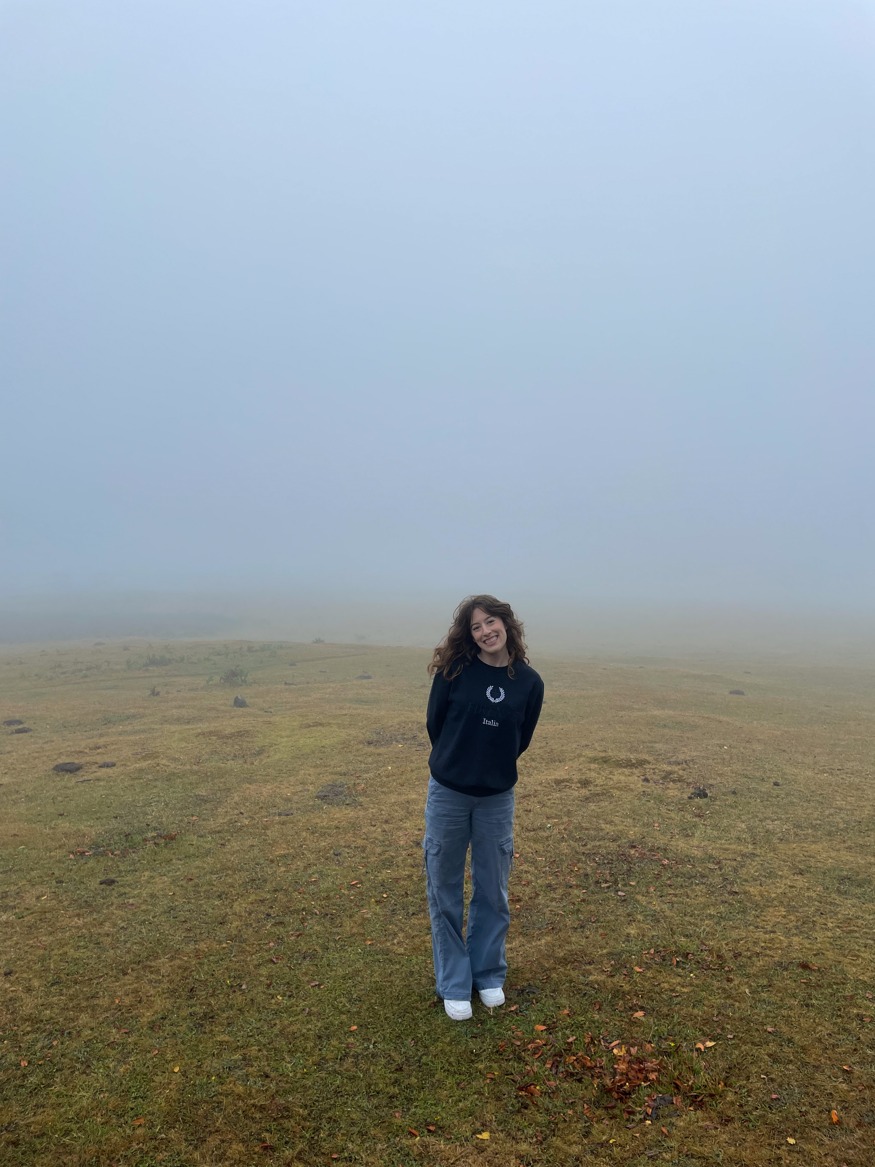 Bella smiling in the Fanal Forest nearly engulfed by fog. Not a single tree is visible in the background due to the thick fog.