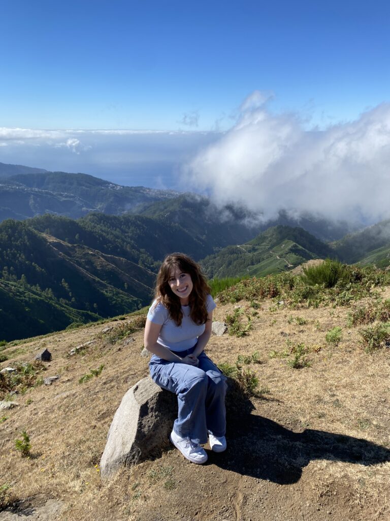 Bella sitting on a rock on a mountaintop with scenic views of the Atlantic Ocean behind her.