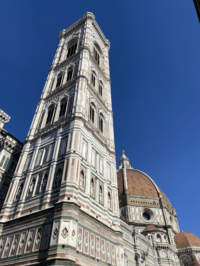 Giotto's Campanile and the orange Duomo behind it set against a bright blue cloudless sky.