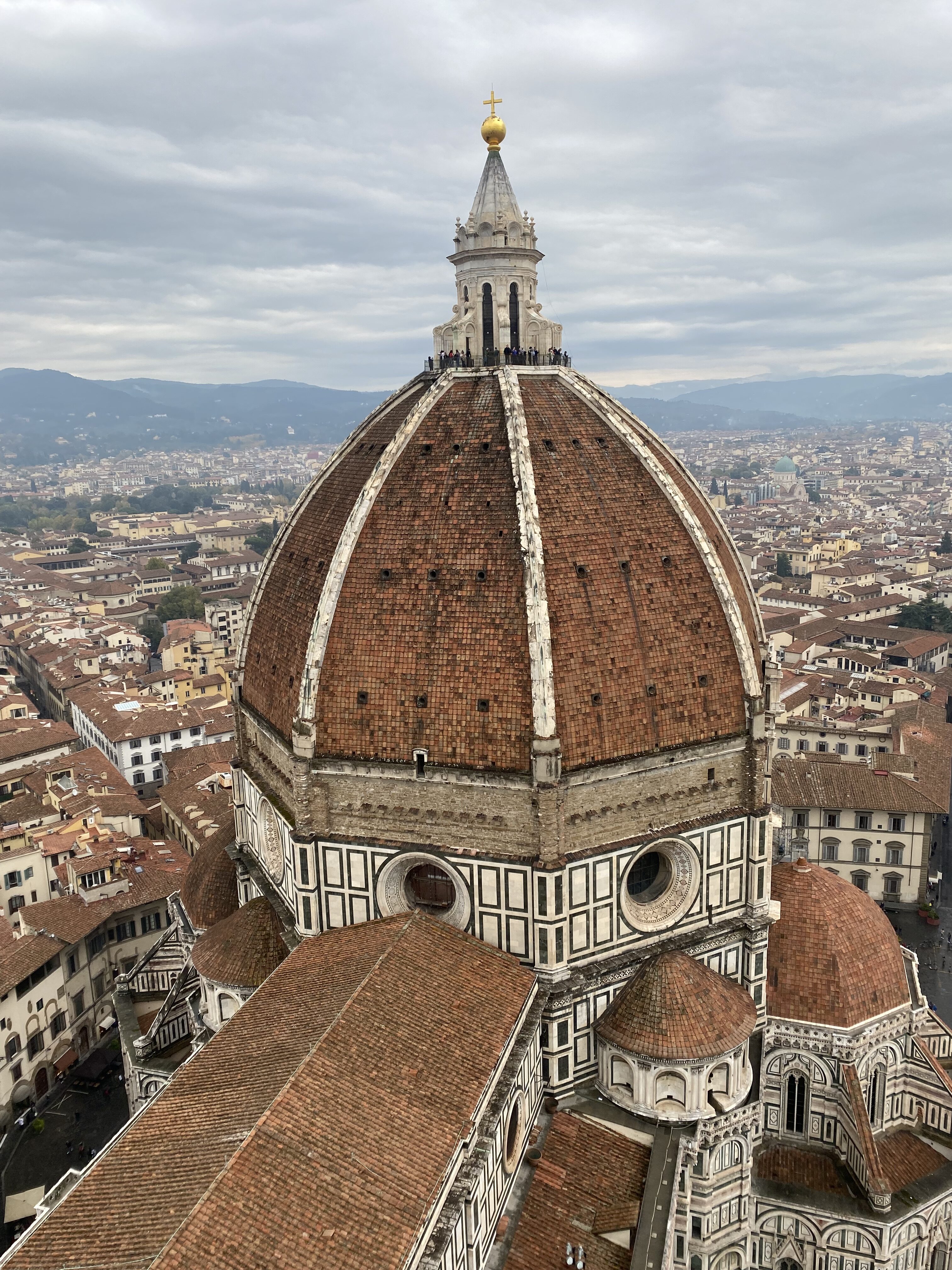 The burnt orange duomo in Florence seen from Giotto's Campanile. The sky is cloudy and orange rooftops of the city can be seen behind the Duomo.