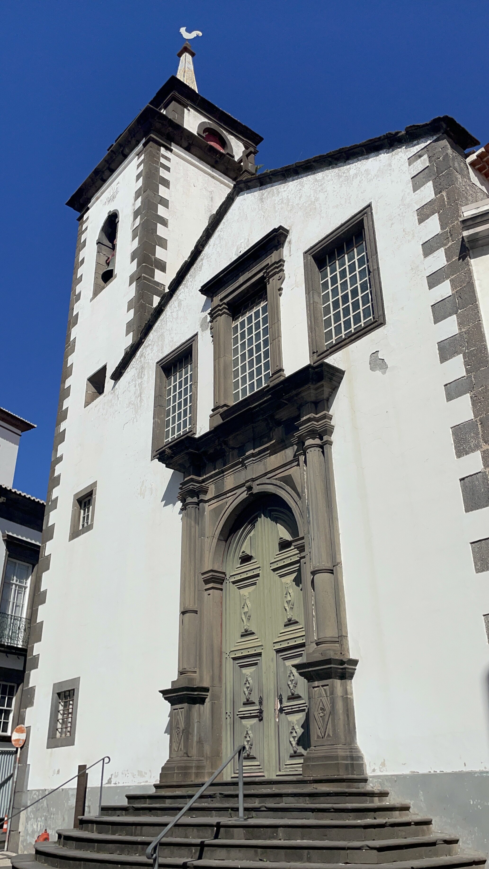 A white and dark stone building with a monumental dark stone door in front of a dark blue sky in Funchal Old town.