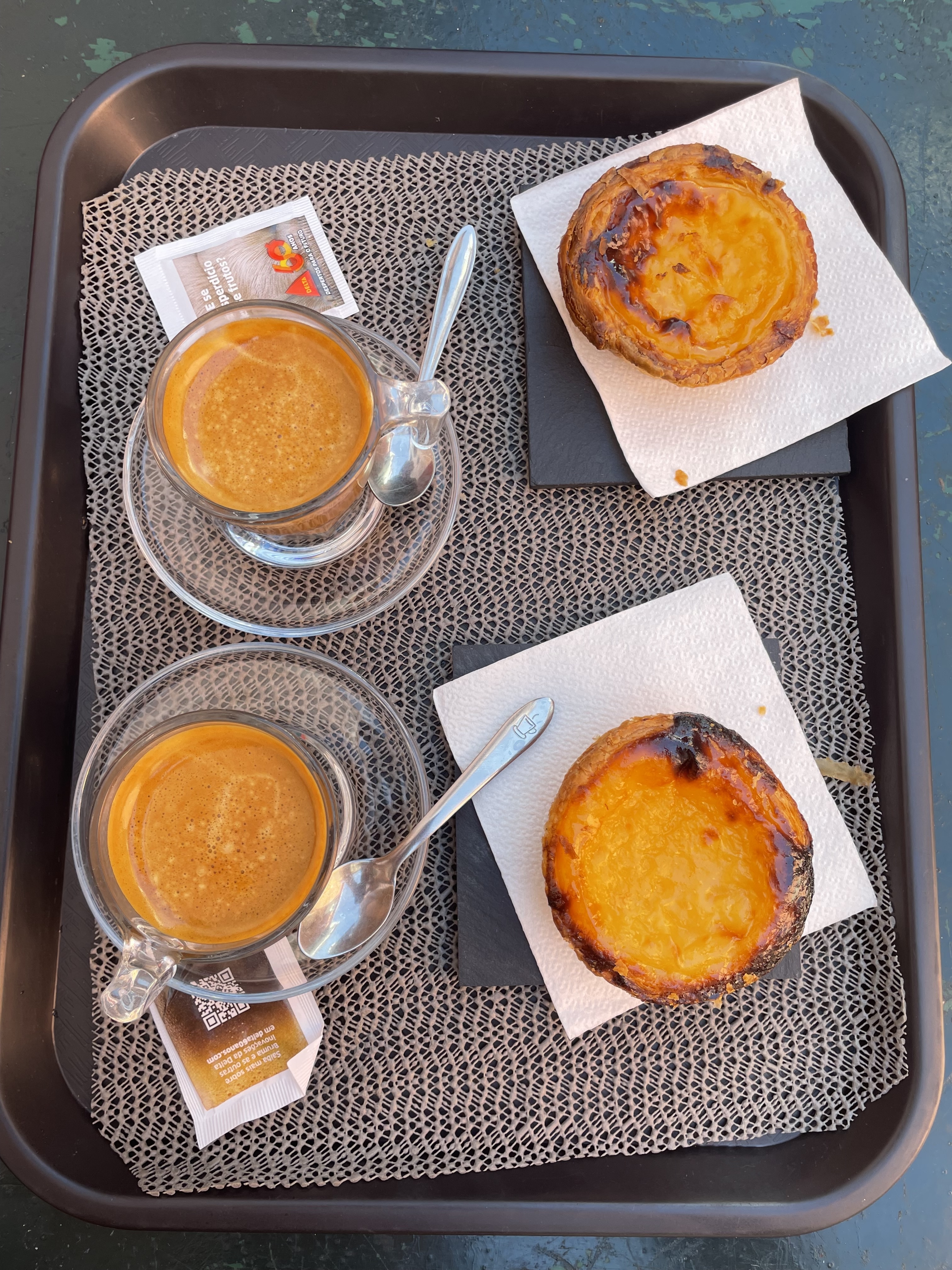 A pair of Madeira coffee and two flaky, crispy Pastéis de Nata on a dark grey tray.