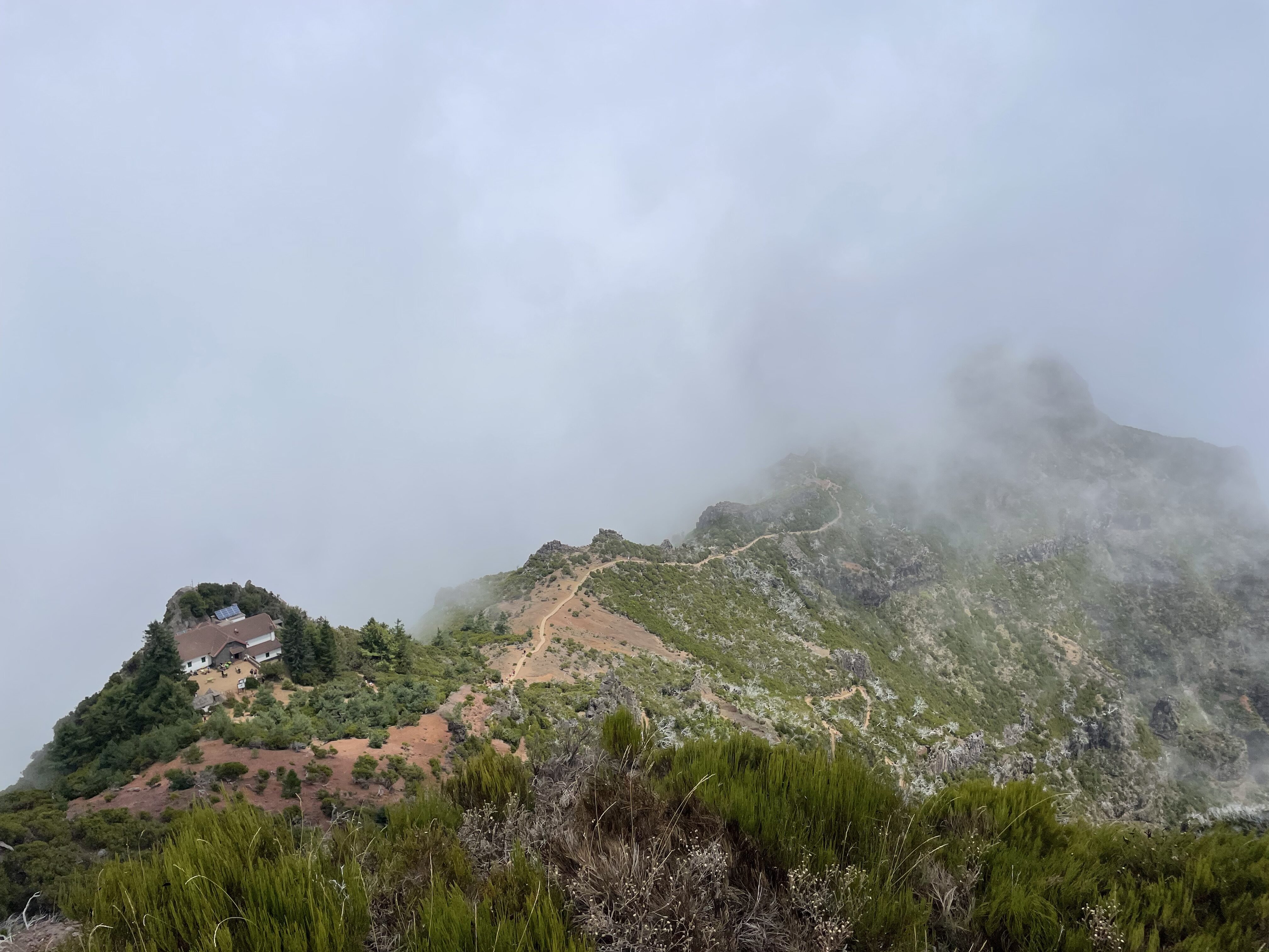A cloud-covered view of the Pico Ruivo trail with a small hut along the trail.