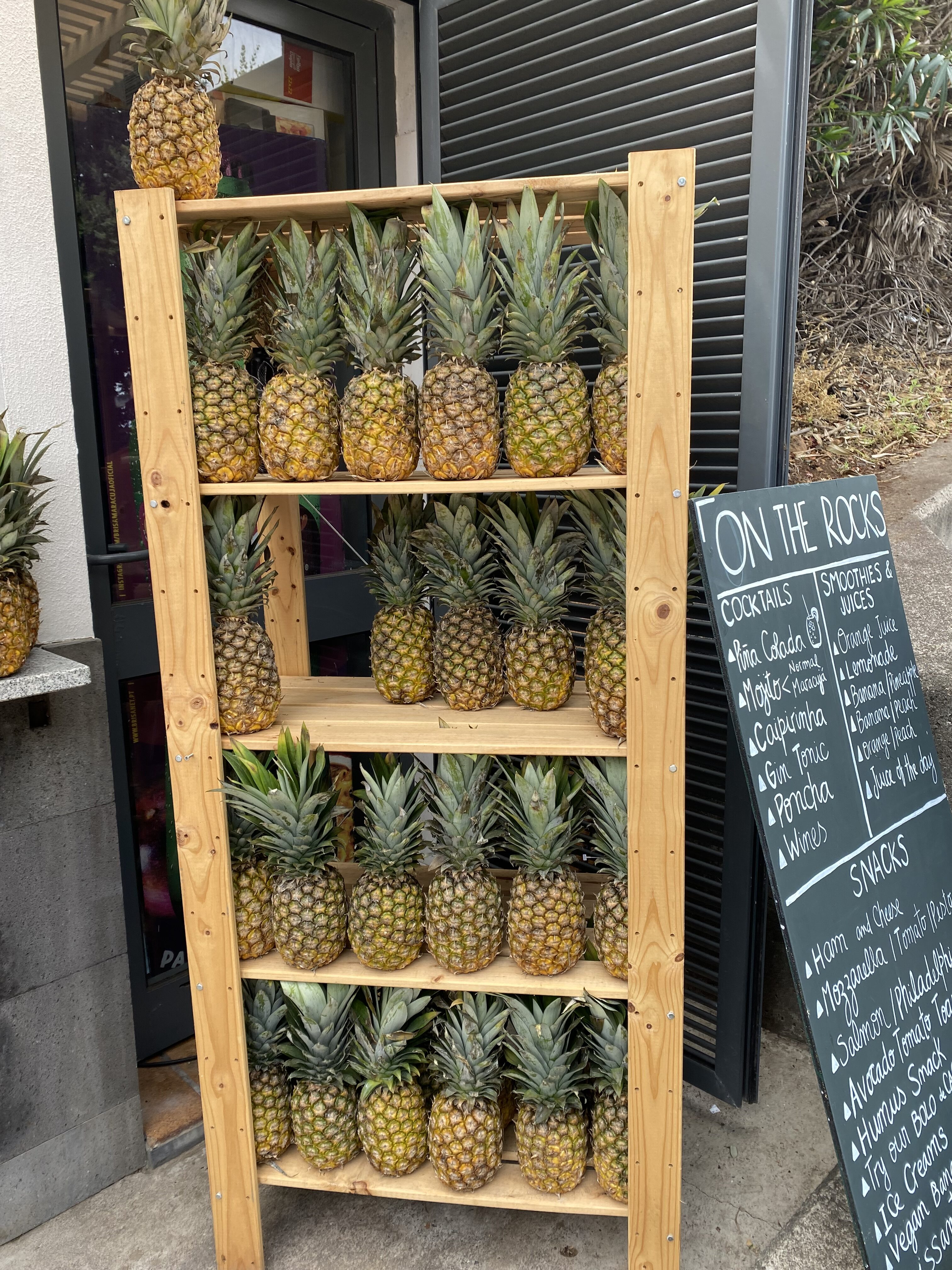 Pineapples stacked on a wooden shelf with a chalkboard sign detailing the various cocktails, smoothies and snacks.