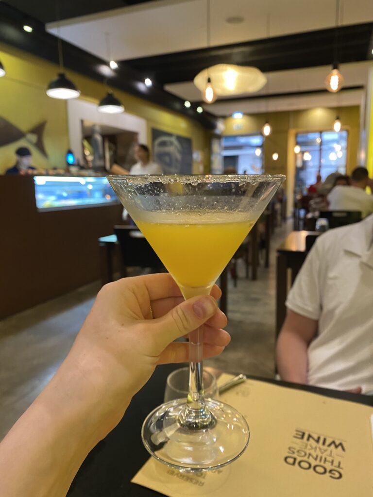 A glass of Poncha, Madeira's traditional boozy punch, with a restaurant scene in the background.
