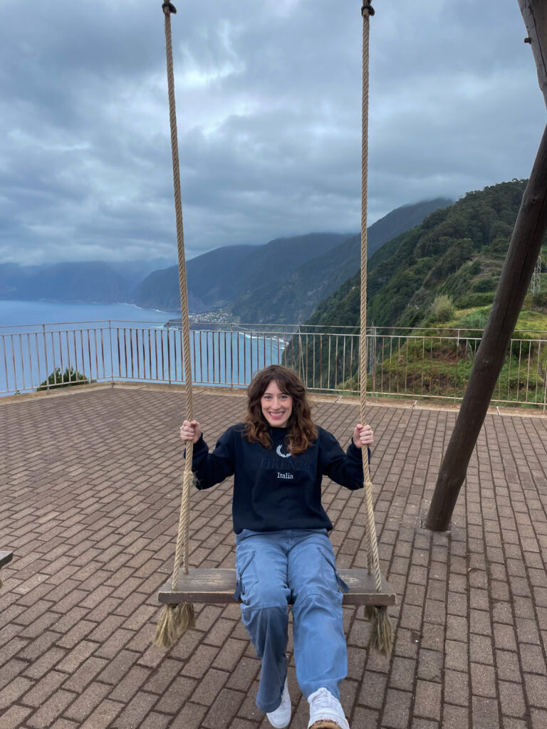Bella on a wooden swing at a viewpoint near Ribeira da Janela with stunning views of the hillsides and the ocean.