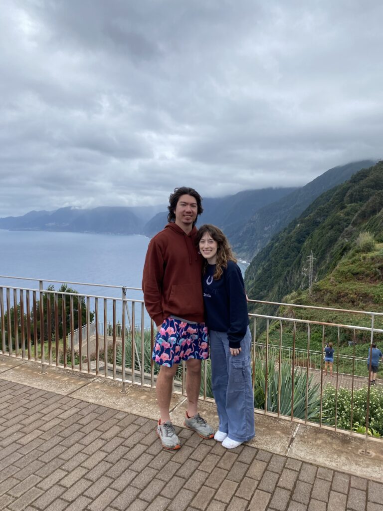 Bella and Sean (her boyfriend) smiling along a railing in Madeira with views of the hillsides and the Atlantic Ocean.