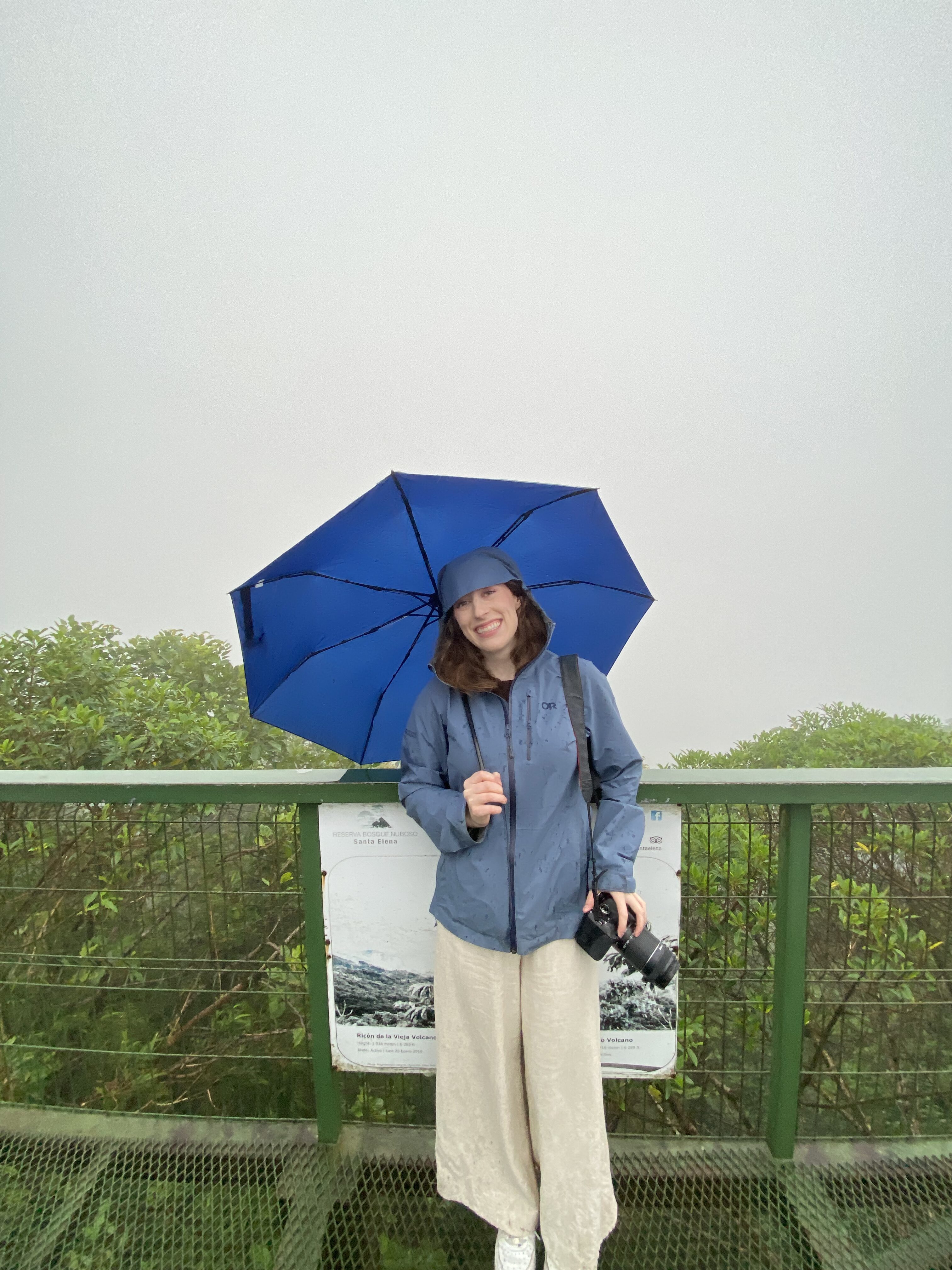 Bella holding a bright blue umbrella at the Santa Elena Cloud Forest, shrouded in fog.