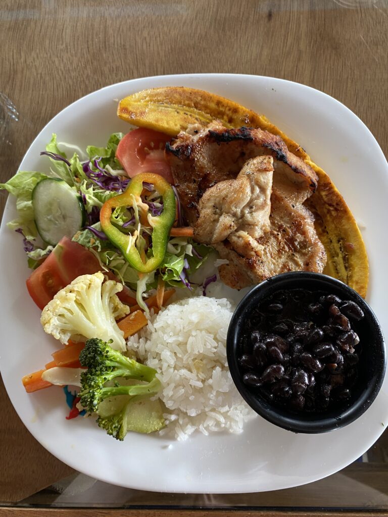 A plate of Costa Rican food, including vegetables, chicken, rice and beans, and plantains.