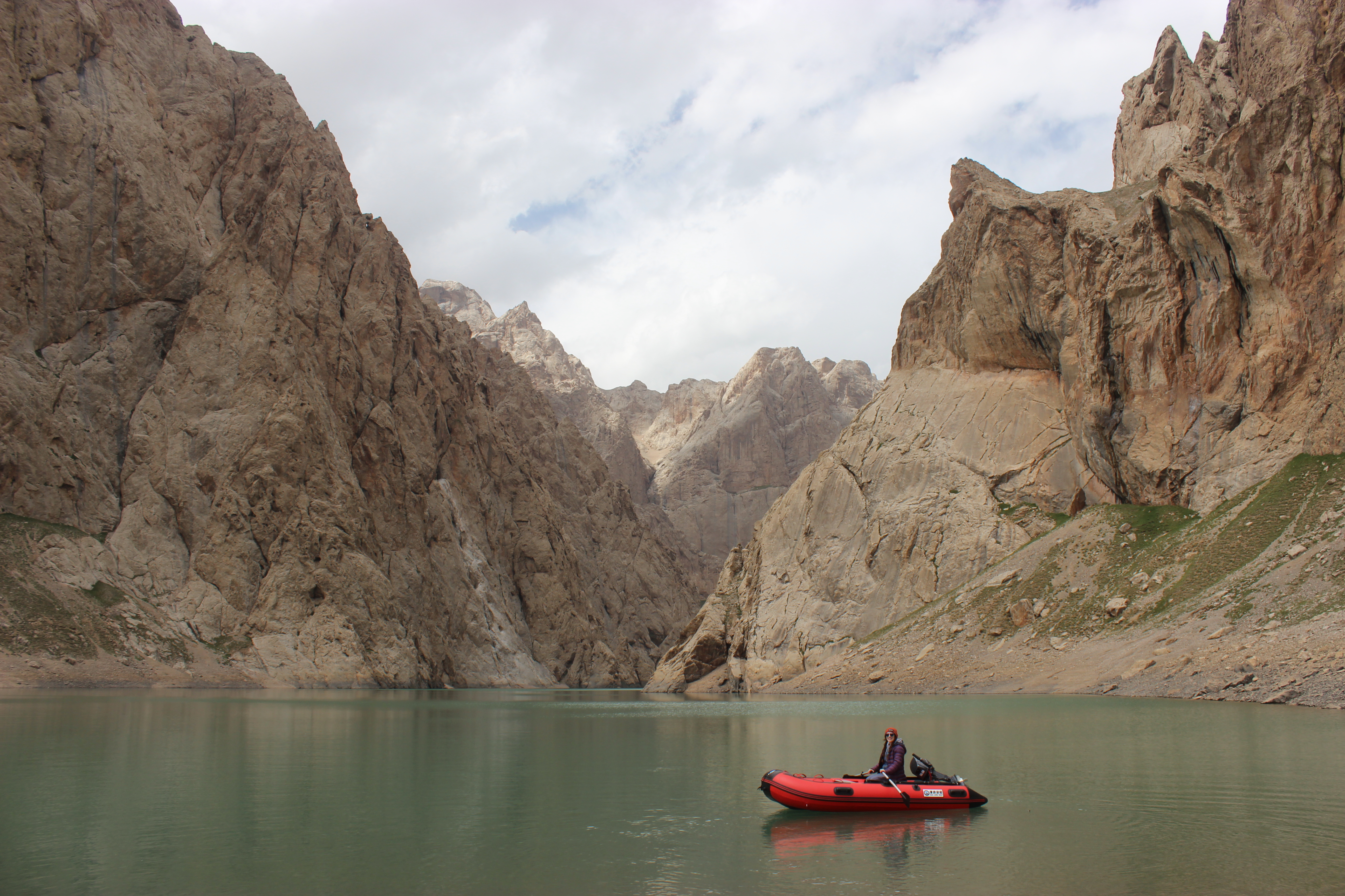 A small red boat in the center of a cloud-covered lake, surrounded by rock formations.