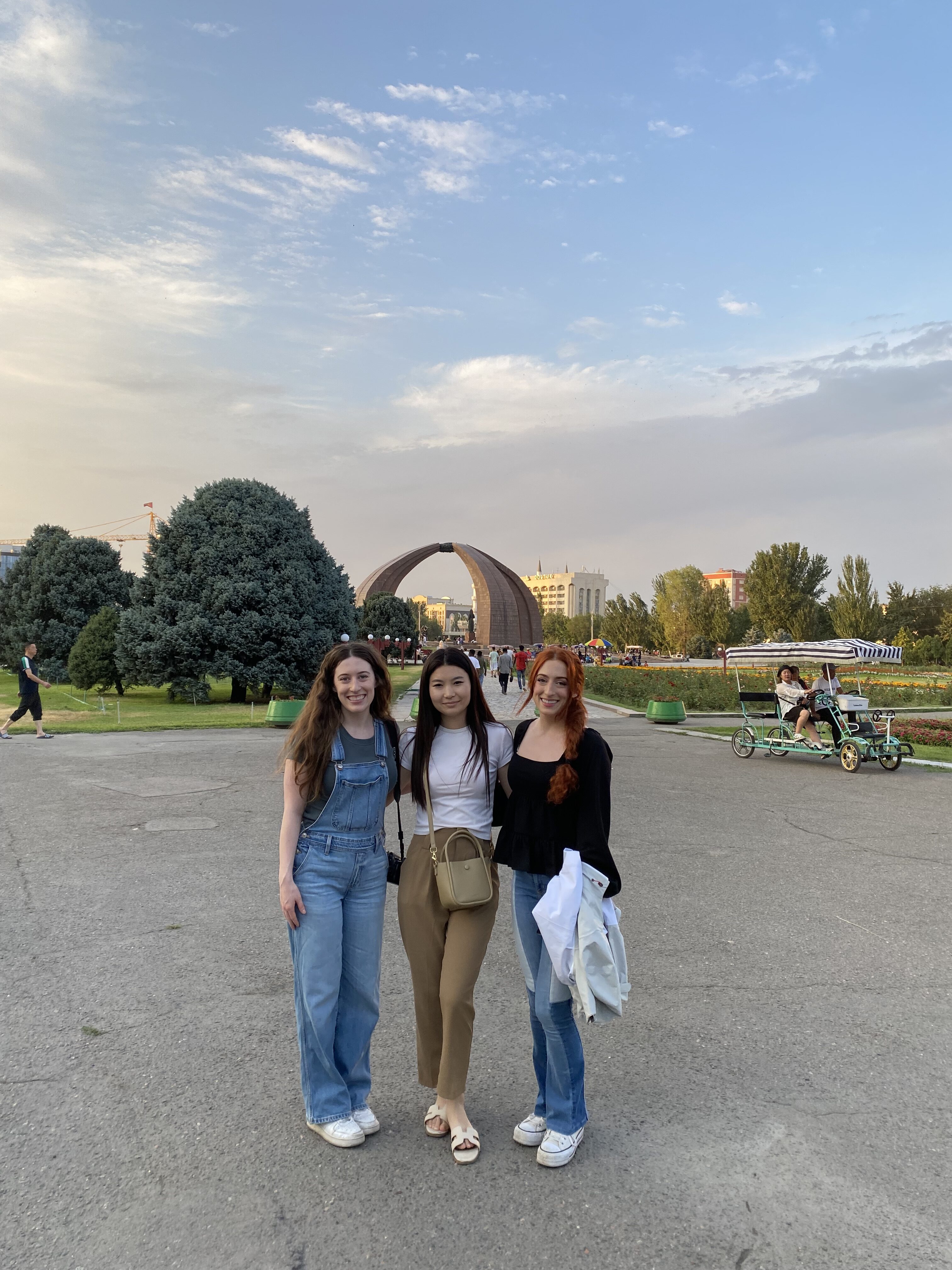 Three beautiful girls standing in front of the Victory Monument in the distance.