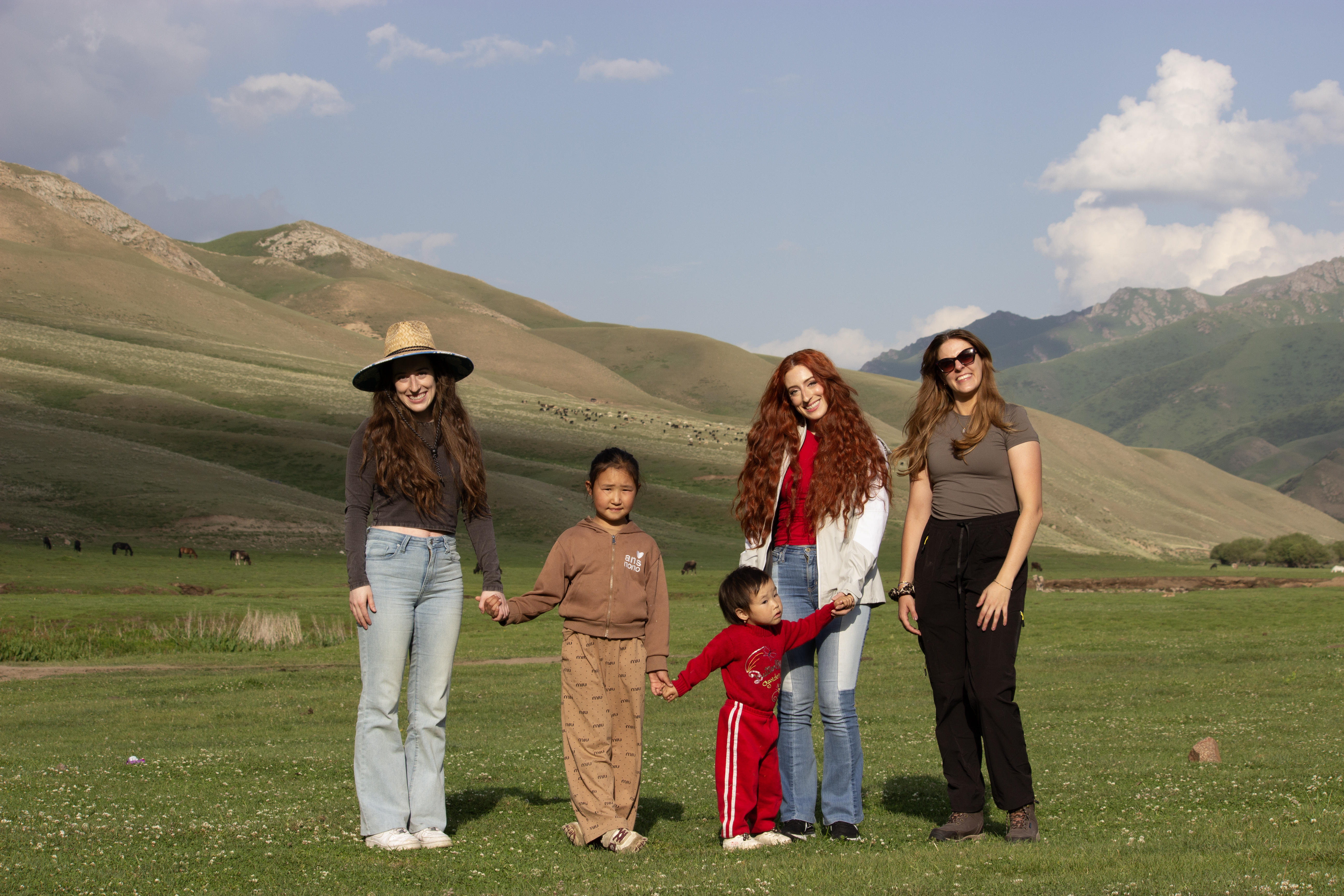 A group of young girls holding the hands of Kyrgyz children in front of a hilly valley.