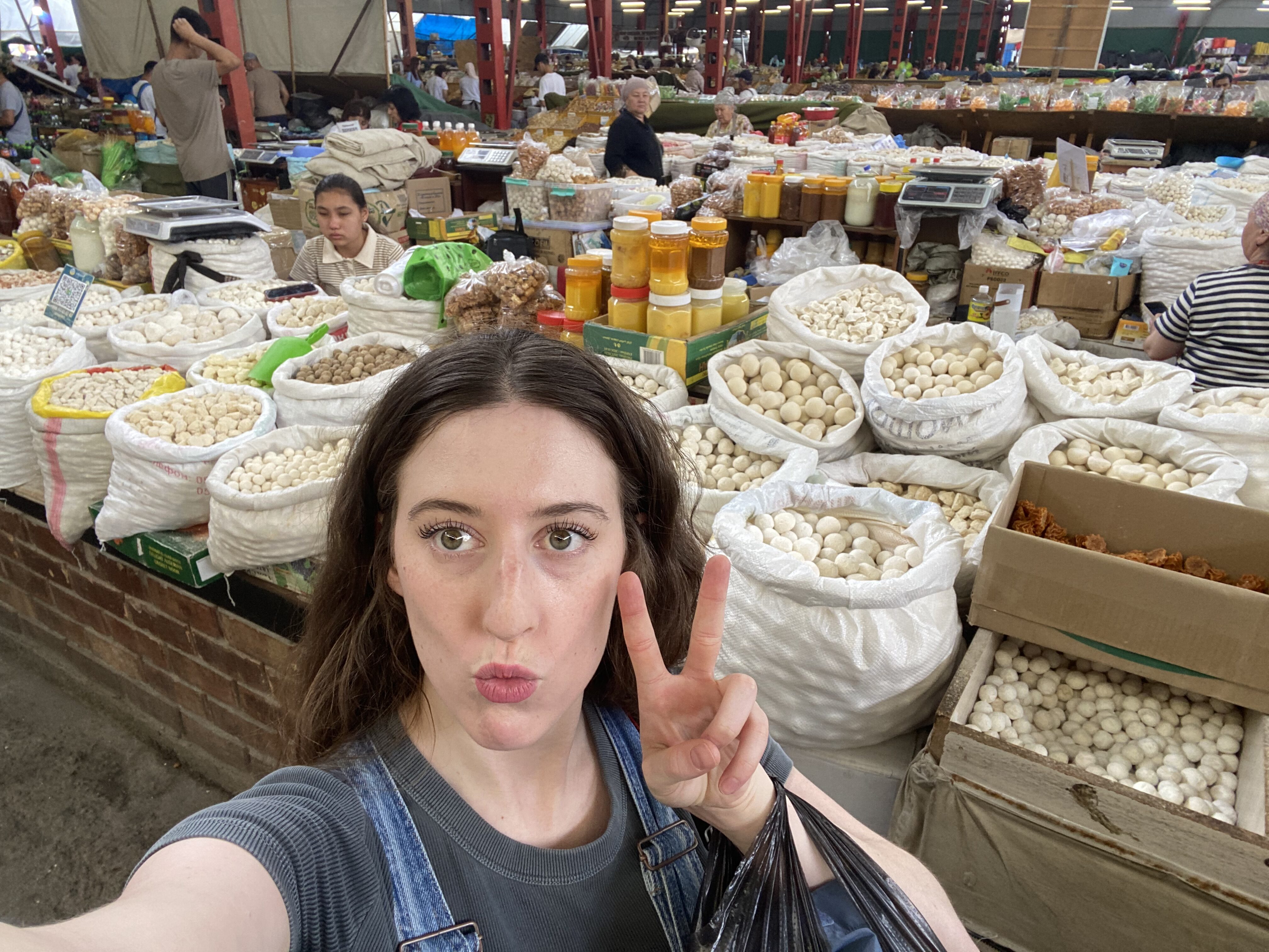 Bella poses for a selfie with a peace sign in front of local Kyrgyz delicacies at the Osh Bazaar.