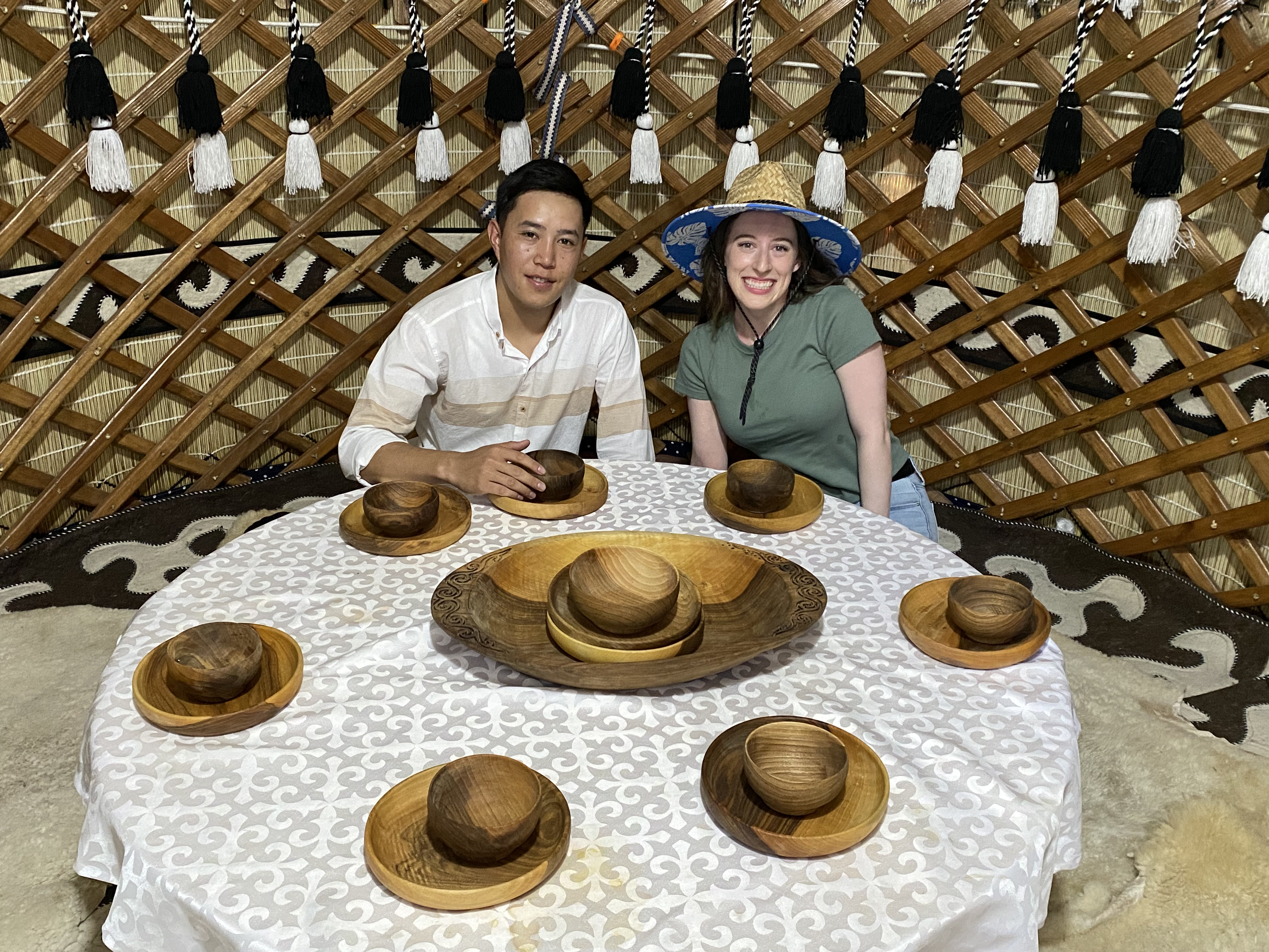 Bella and her local Kyrgyz friend (Suiunbek) sitting around a table in a yurt with wooden bowls and plates.