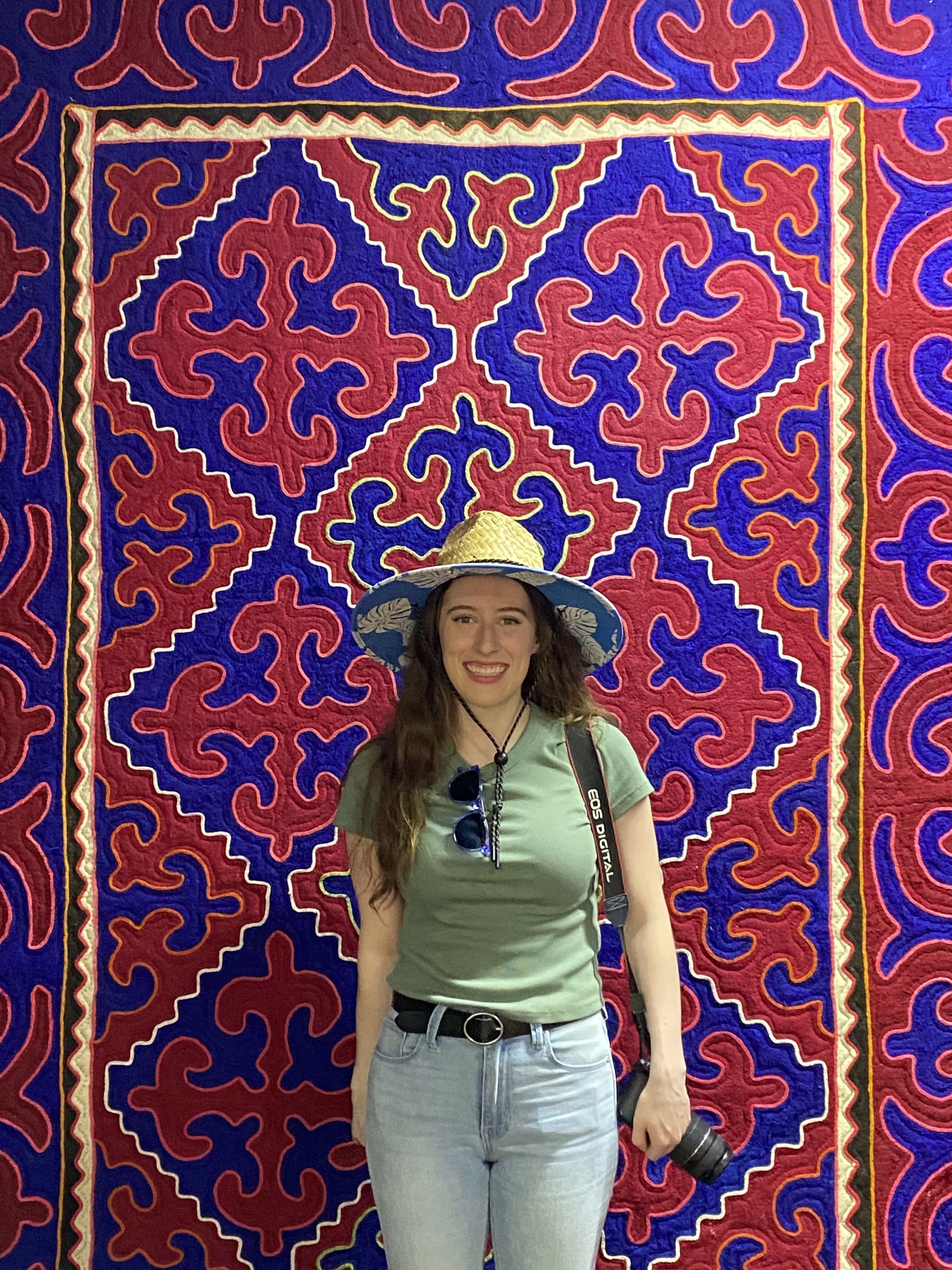 Bella in front of a colorful red and blue Kyrgyz carpet at the State History Museum of Kyrgyzstan.