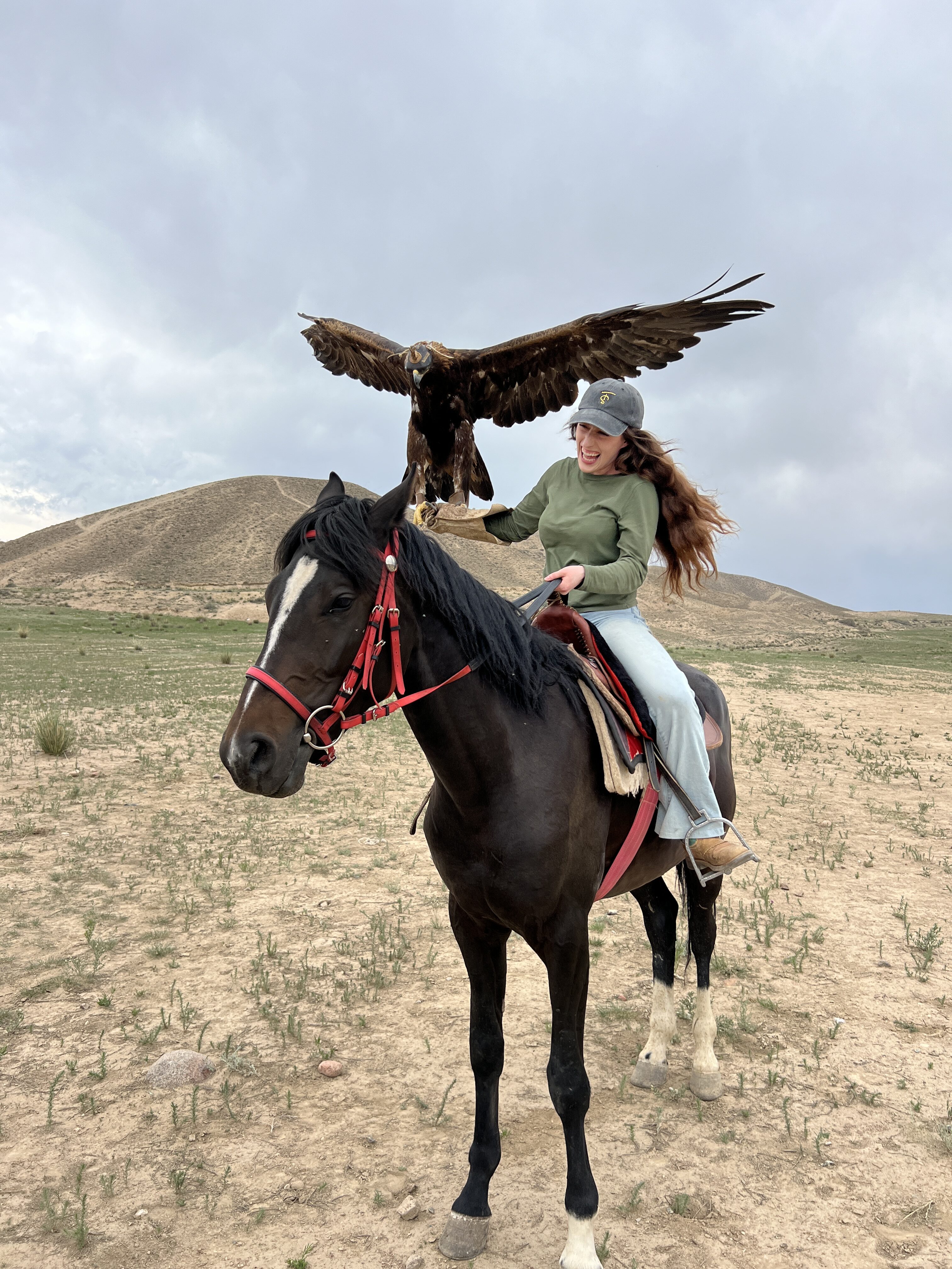Bella holding a eagle spreading its wings, atop a beautiful dark brown horse.